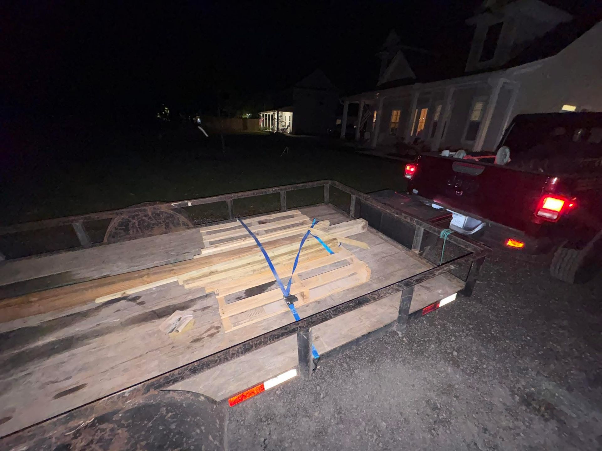 Trailer loaded with lumber beside a car at night in a driveway