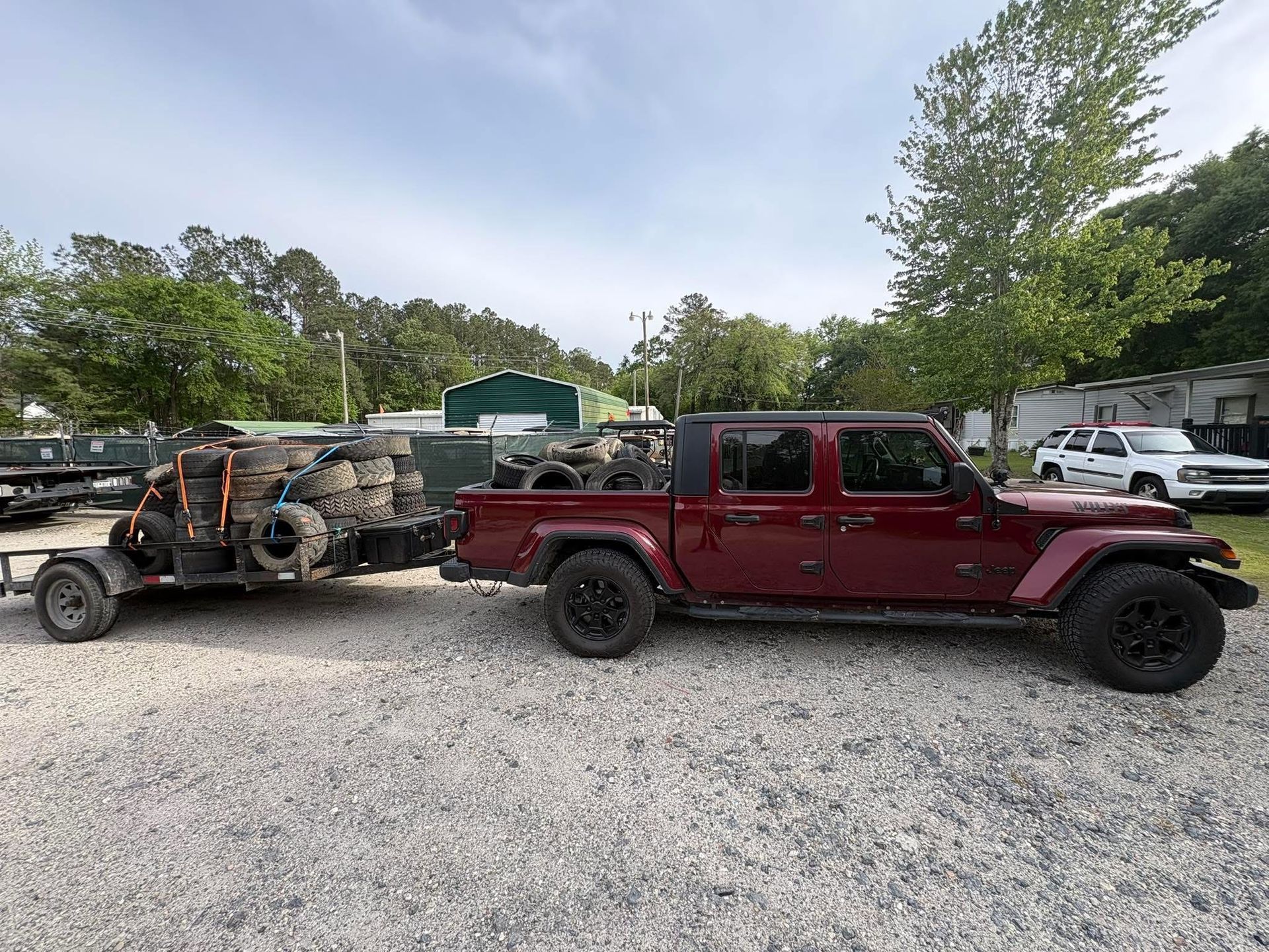 Red pickup truck and off-road buggy parked on gravel lot with trees and vehicles in the background