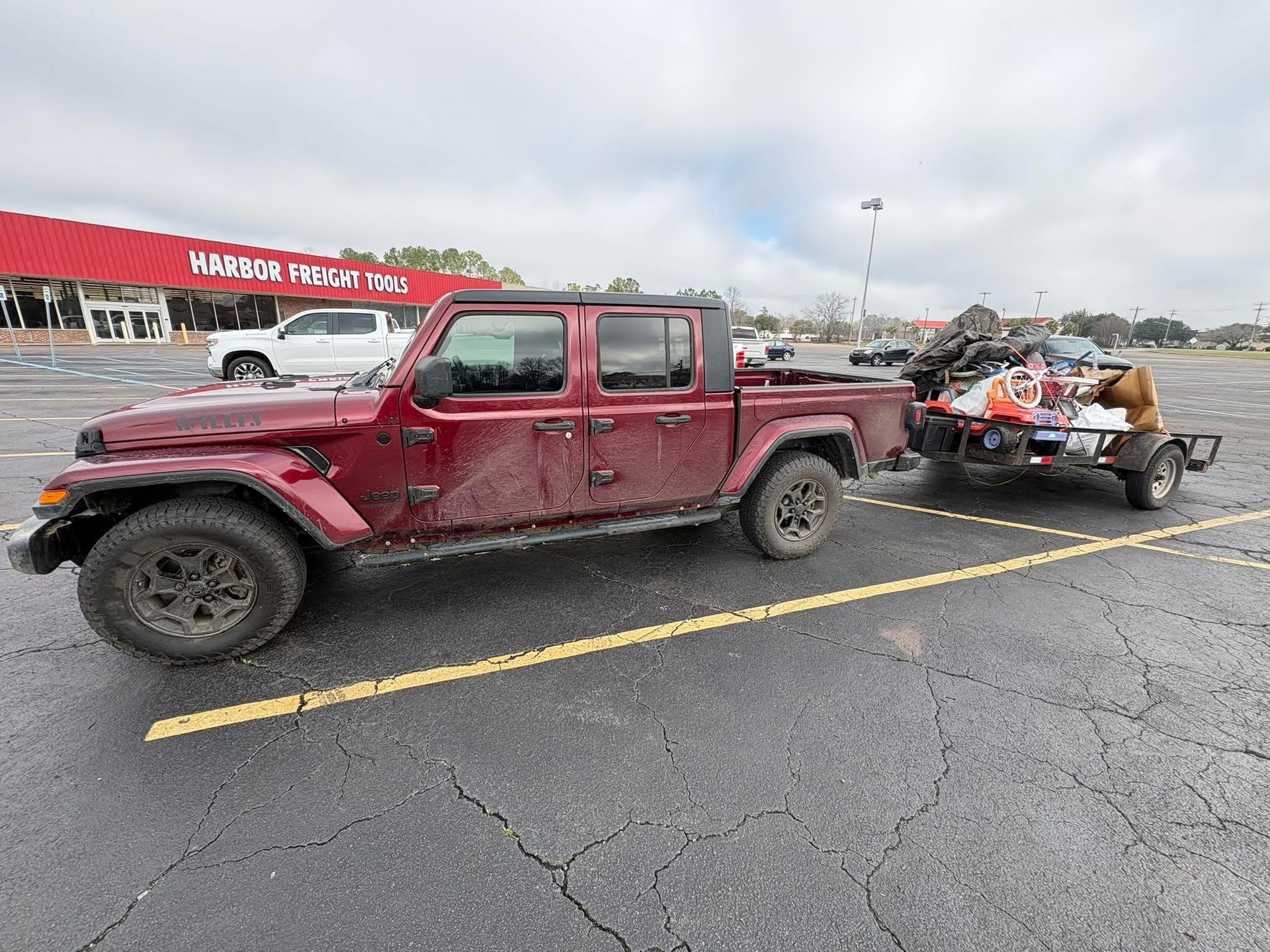 Red pickup truck towing a small trailer loaded with debris in a parking lot.