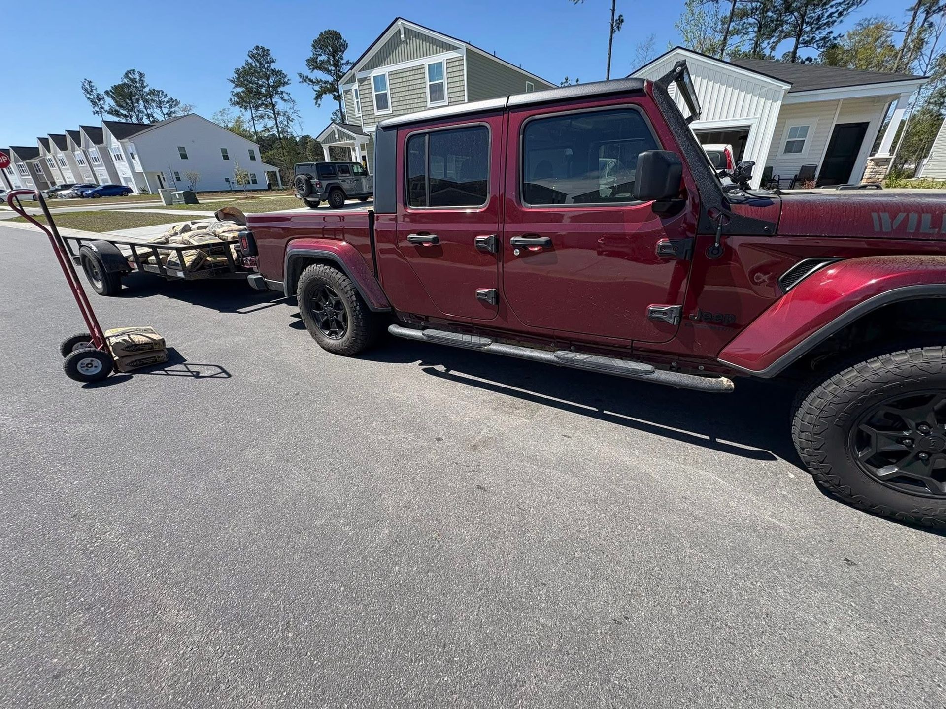 Red pickup truck towing a trailer in a sunny residential street with houses nearby