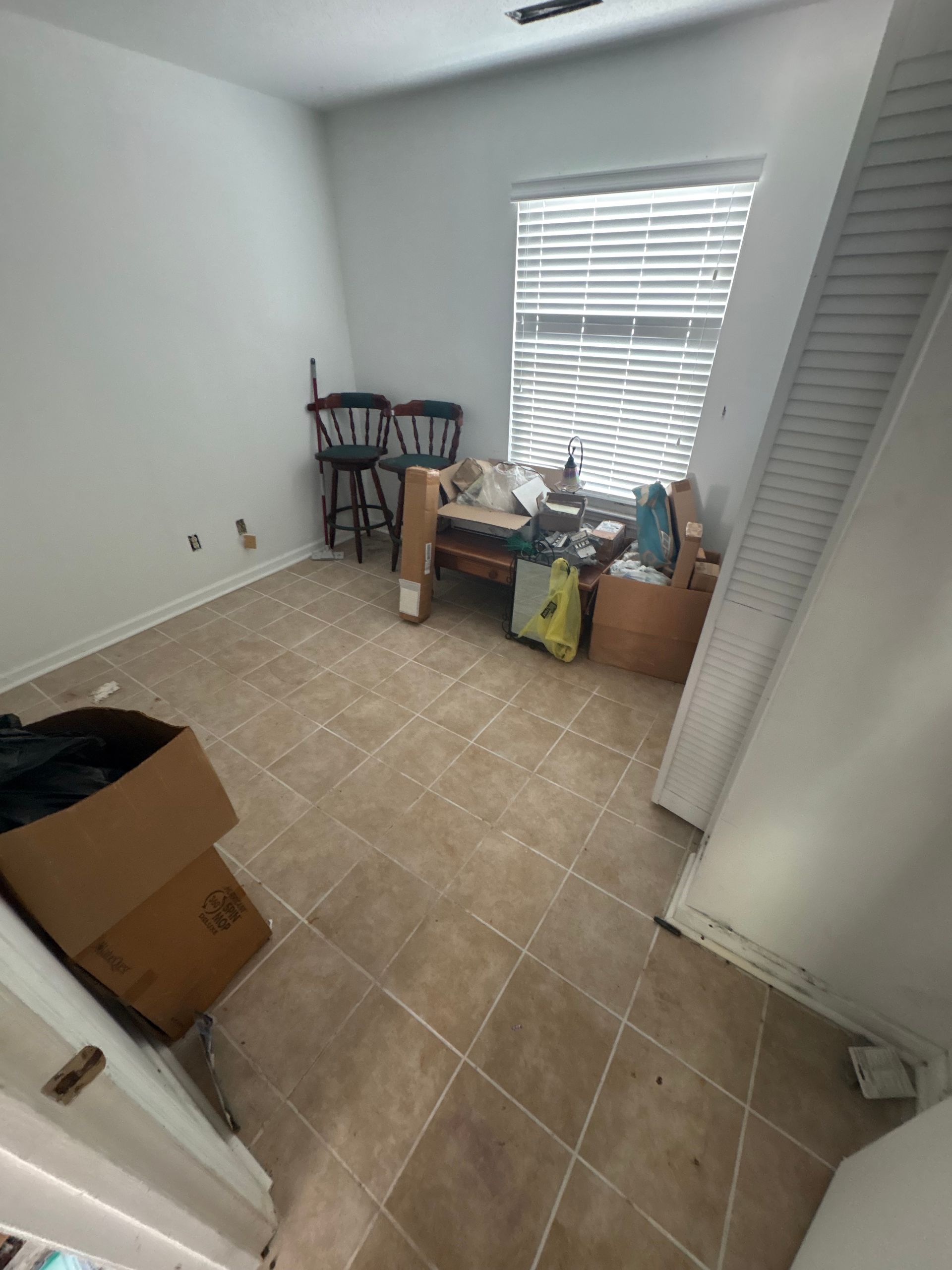 Small empty room with tile floor, boxes, and a table near a window with blinds.