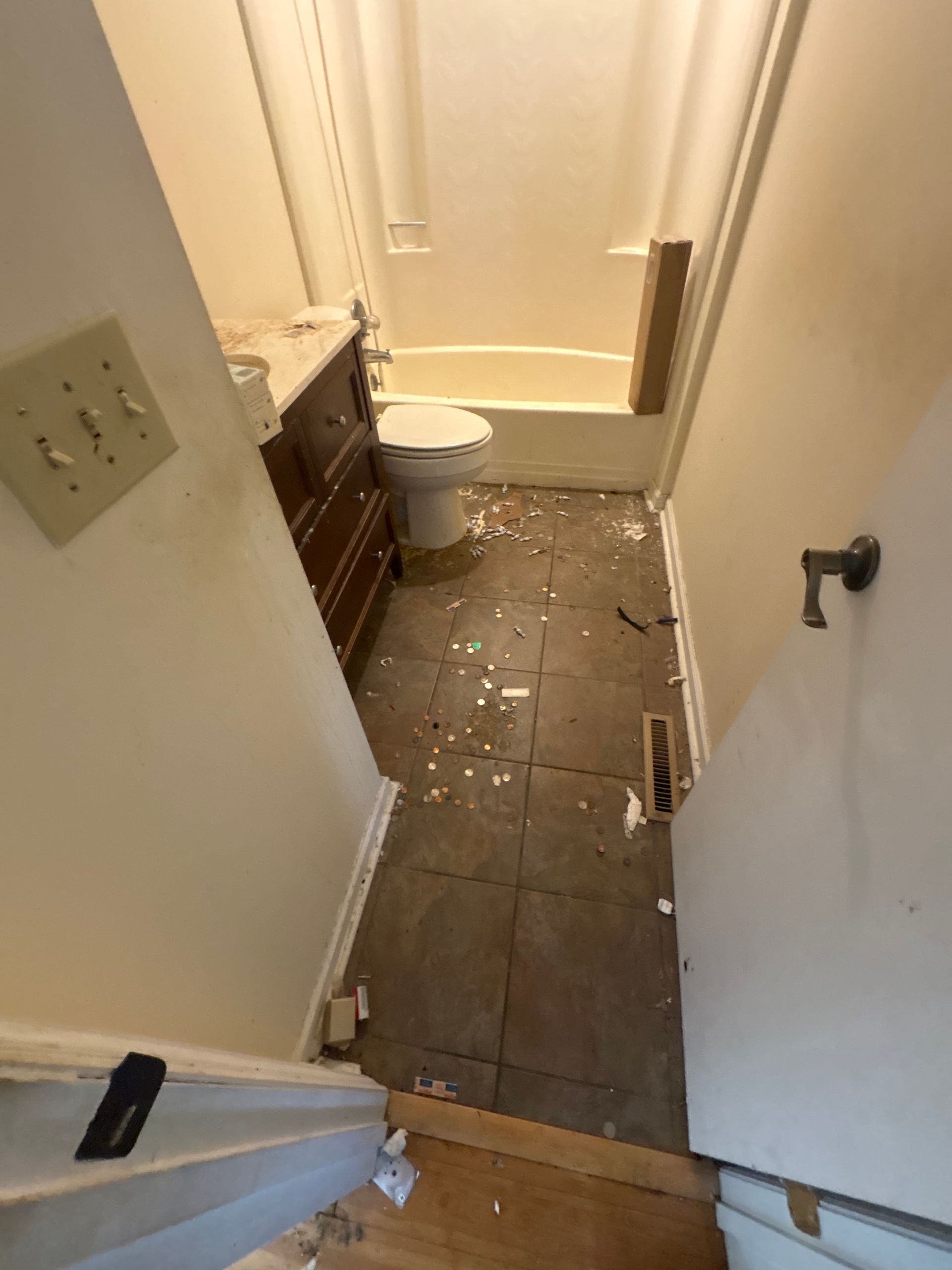 Small bathroom with a damaged tile floor and scattered debris near the toilet and shower.