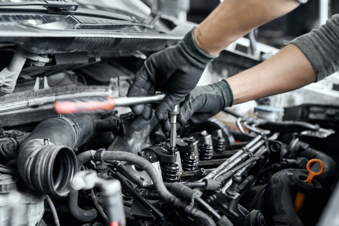 Mechanic working under a car hood, repairing engine components with tools and gloved hands