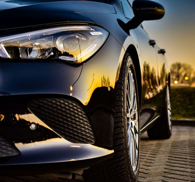 Close-up of a black car’s front headlight and grille at sunset on a paved road