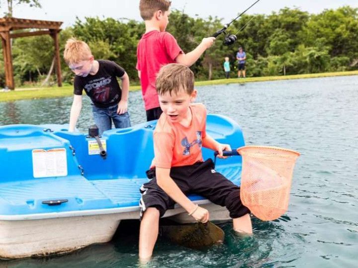 Boys fishing from a blue paddle boat in a pond; one holds a net.