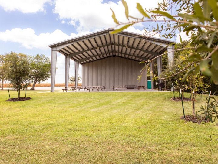 A metal-framed pavilion with a sloped roof sits on a grassy area; benches are inside.
