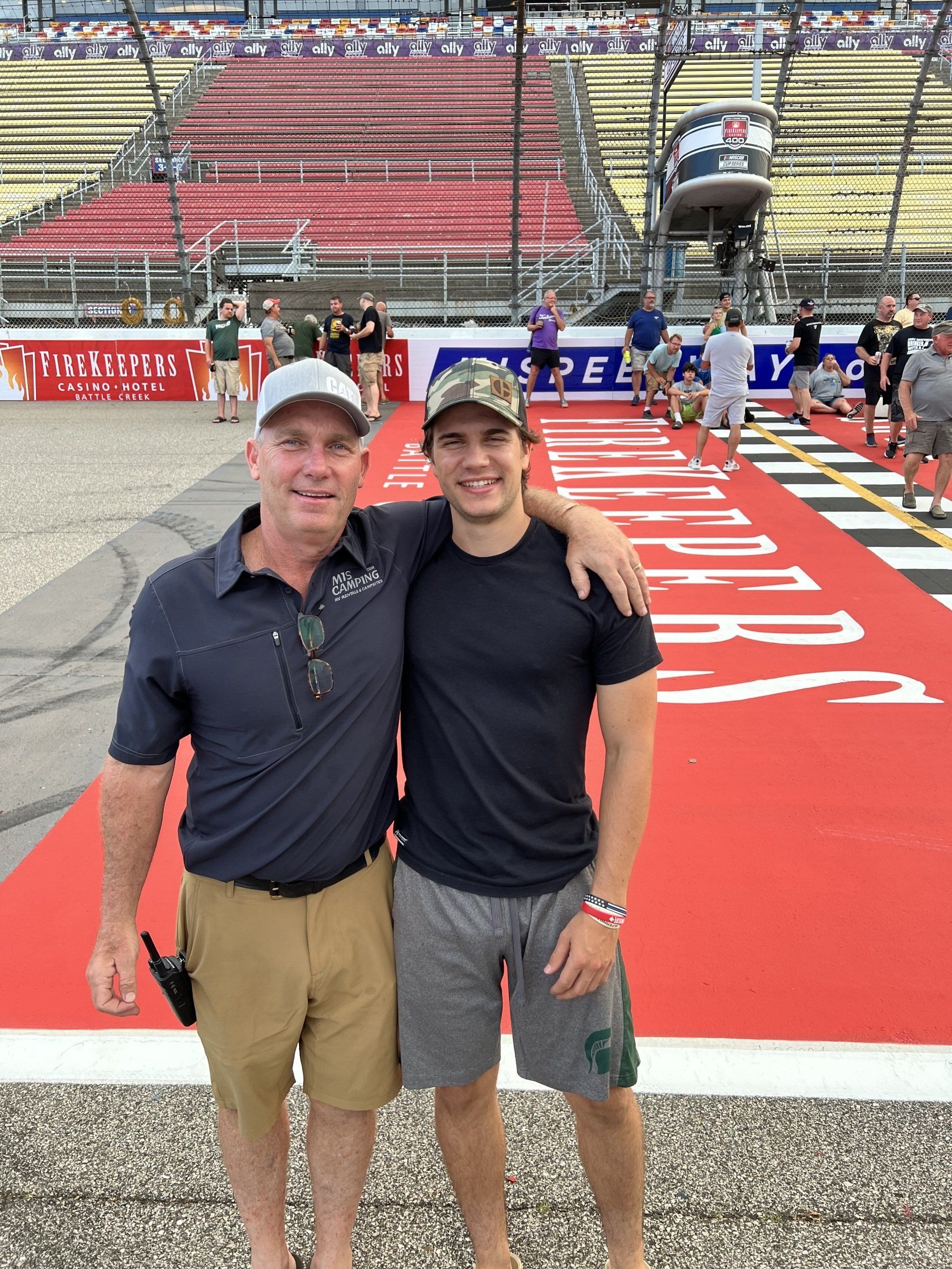 Two men are posing for a picture in front of a race track