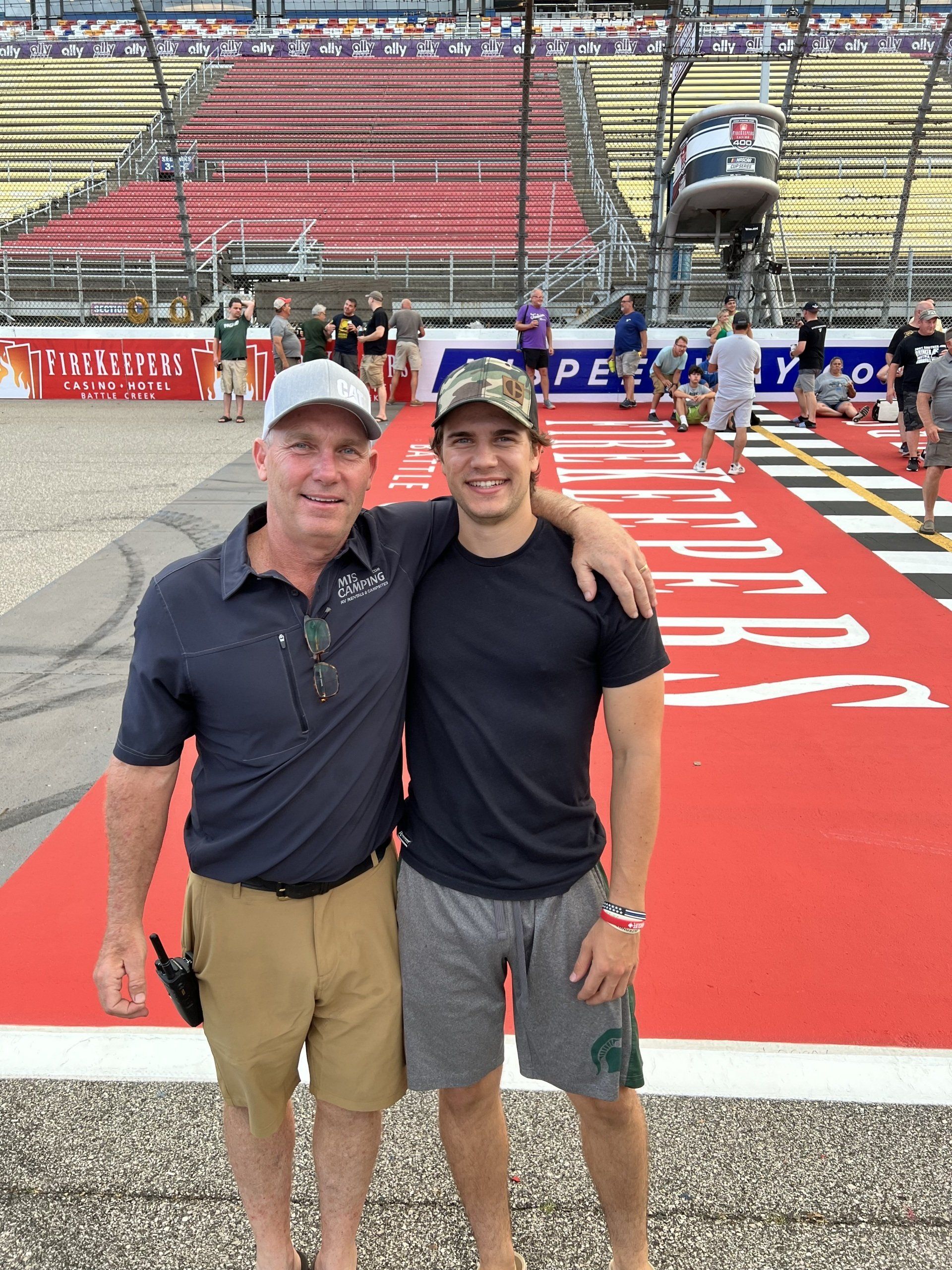 Two men are posing for a picture in front of a race track.