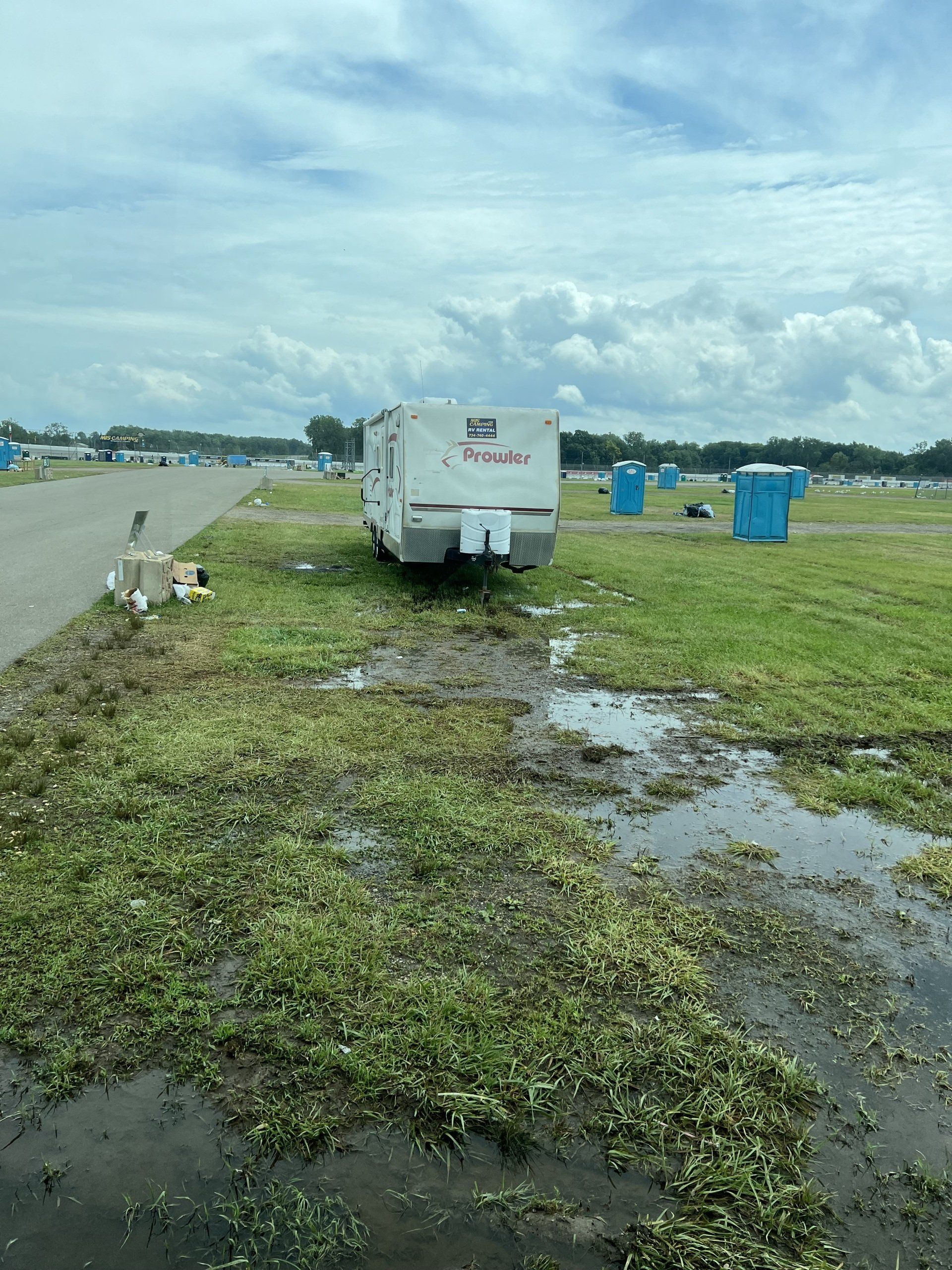 A trailer is parked in a muddy field next to a road.