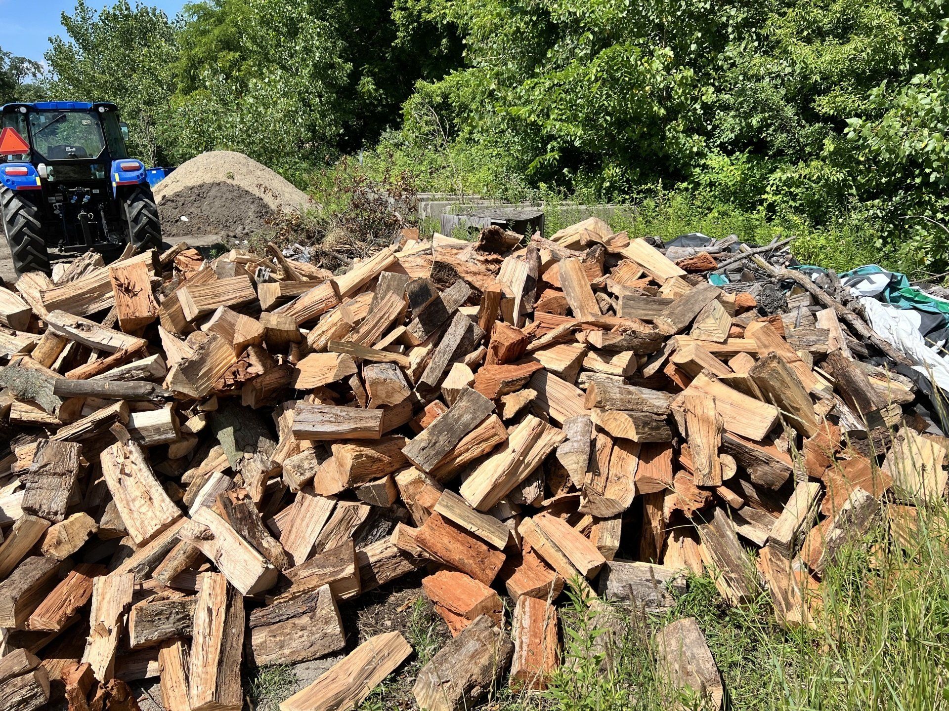 A pile of logs with a tractor in the background.