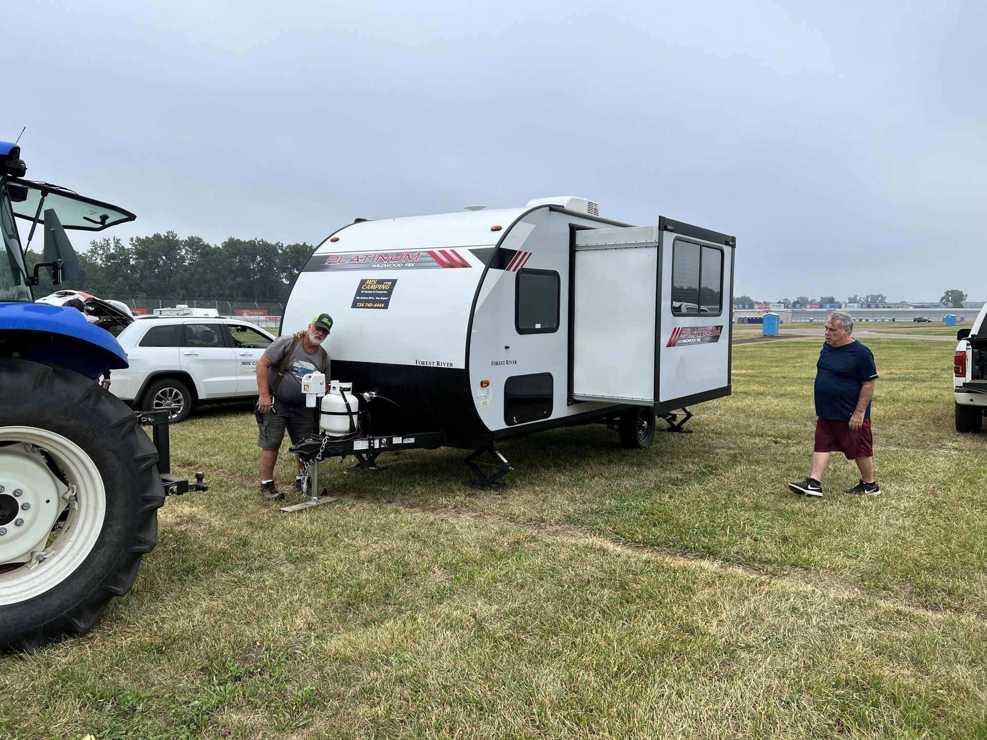 A man is standing next to a trailer in a field.