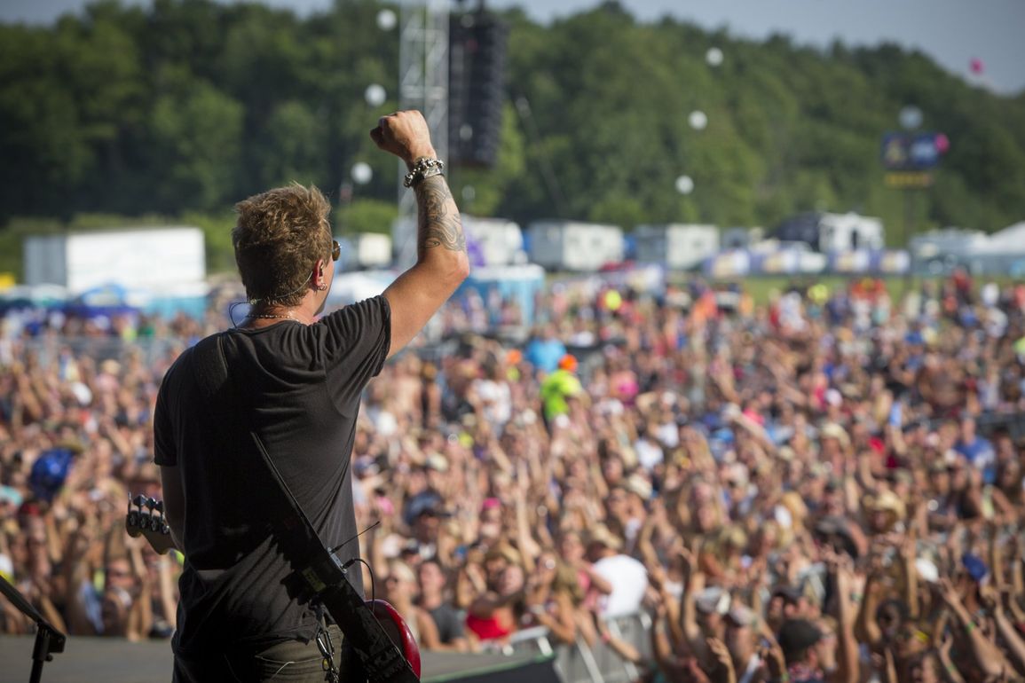A man is playing a guitar in front of a crowd at a music festival.