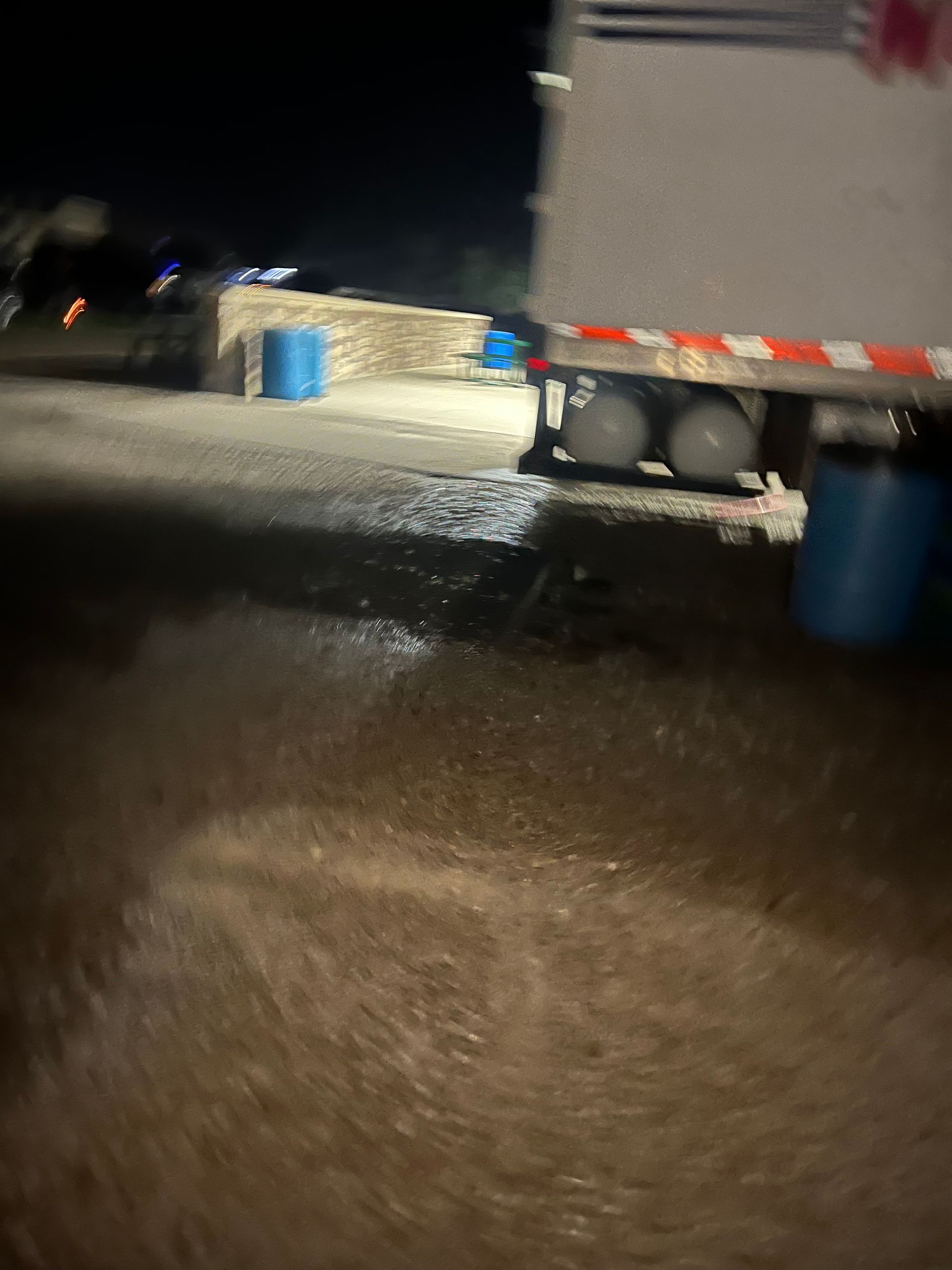 Night shot of a truck with two propane tanks, blue barrels, and wet asphalt.