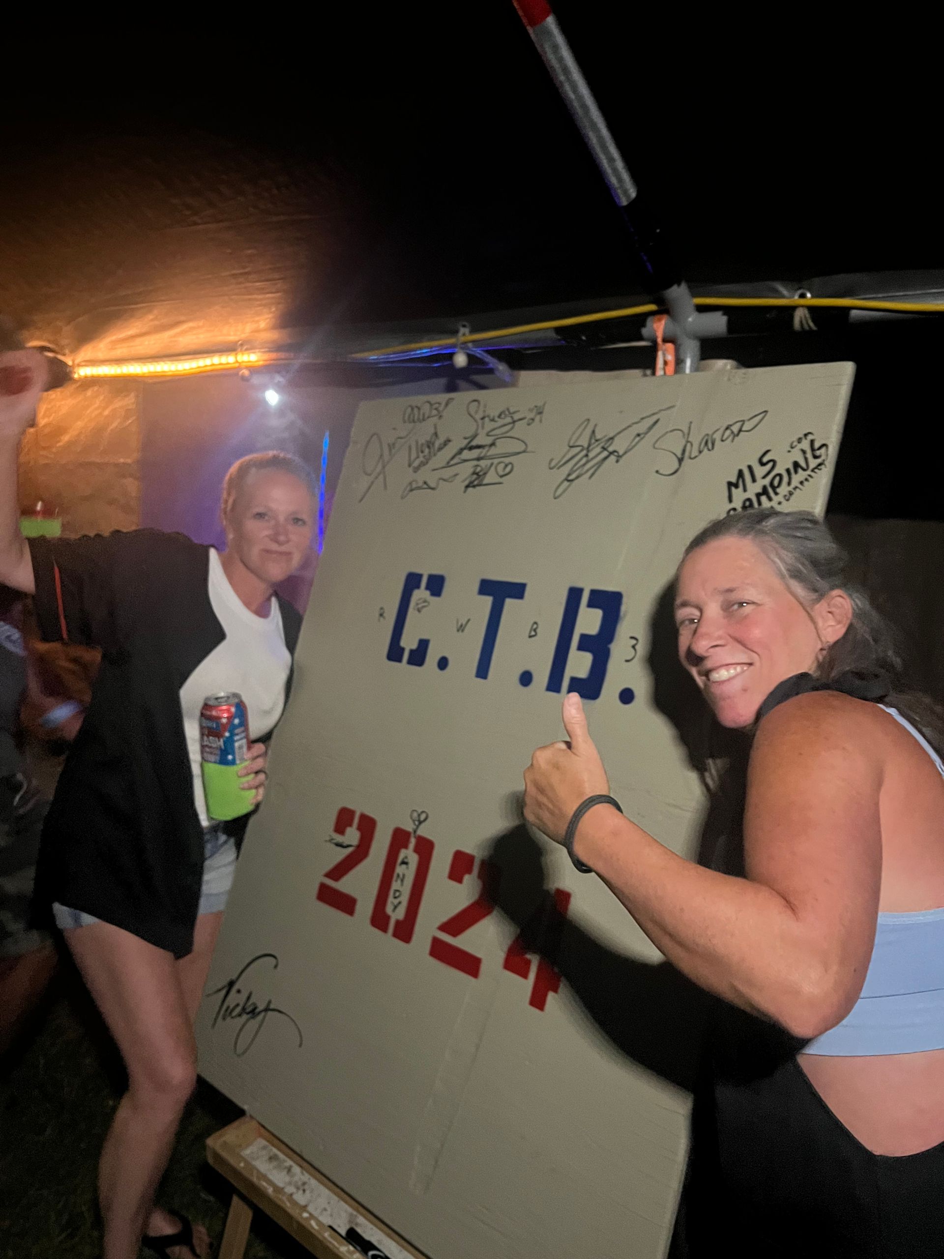 Two women stand by a sign that reads 