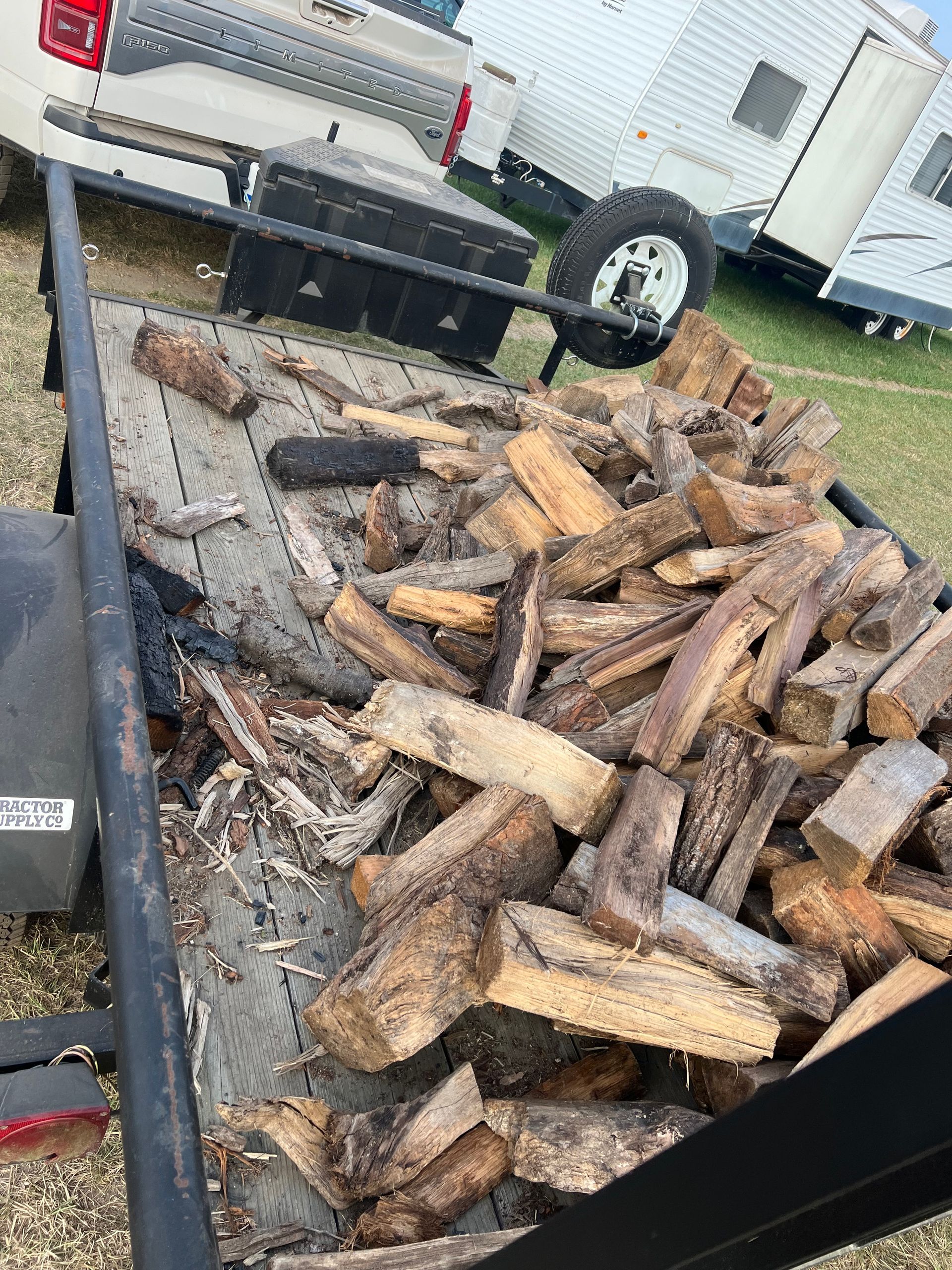 Firewood stacked in a trailer, outdoors. Gray metal trailer with a black frame, daylight.