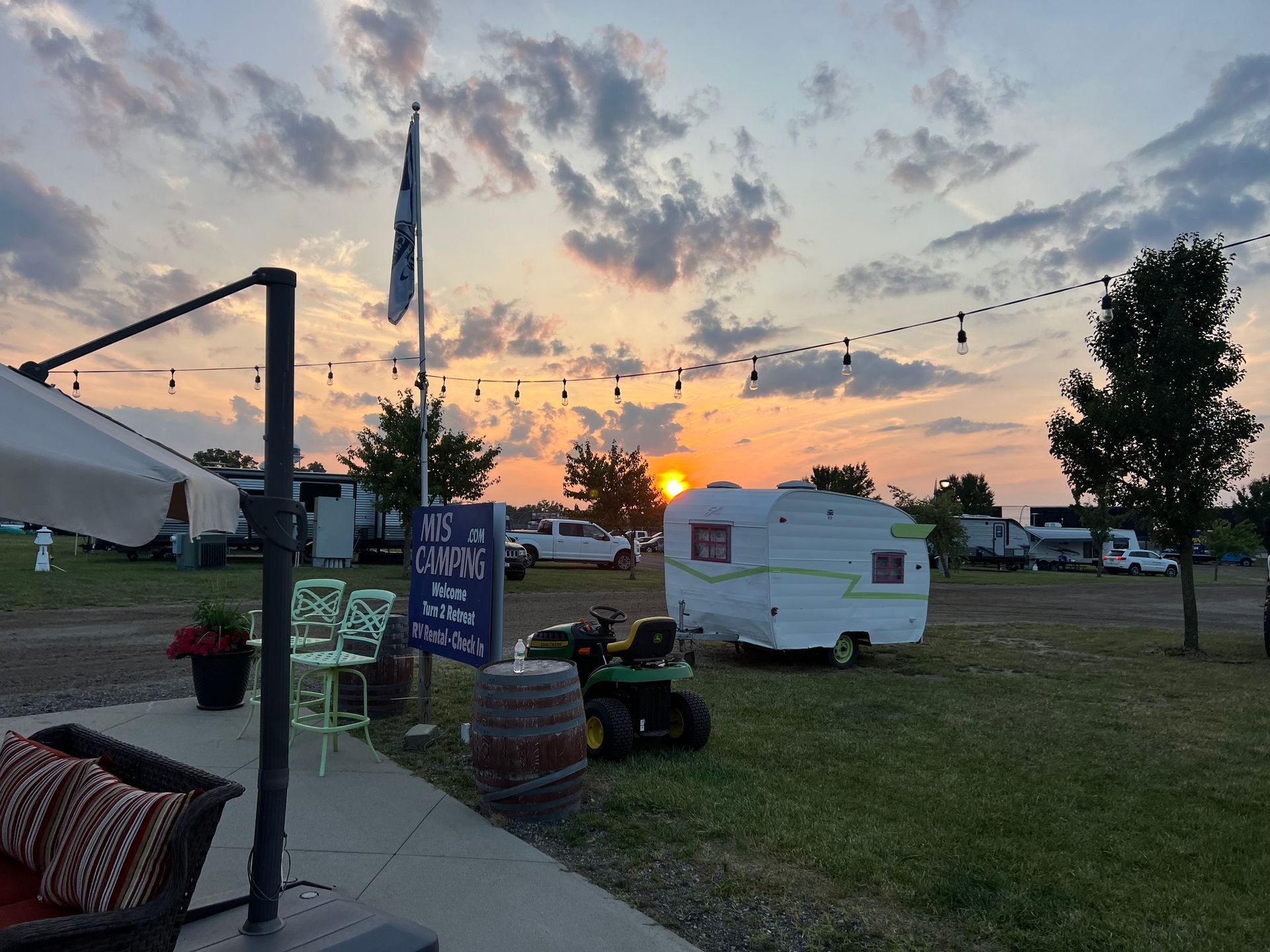 Sunset over a campsite with RVs, string lights, and a white camper.