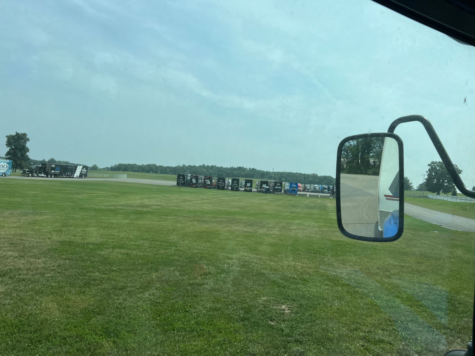 View from vehicle window of a grassy field with structures and a side mirror.