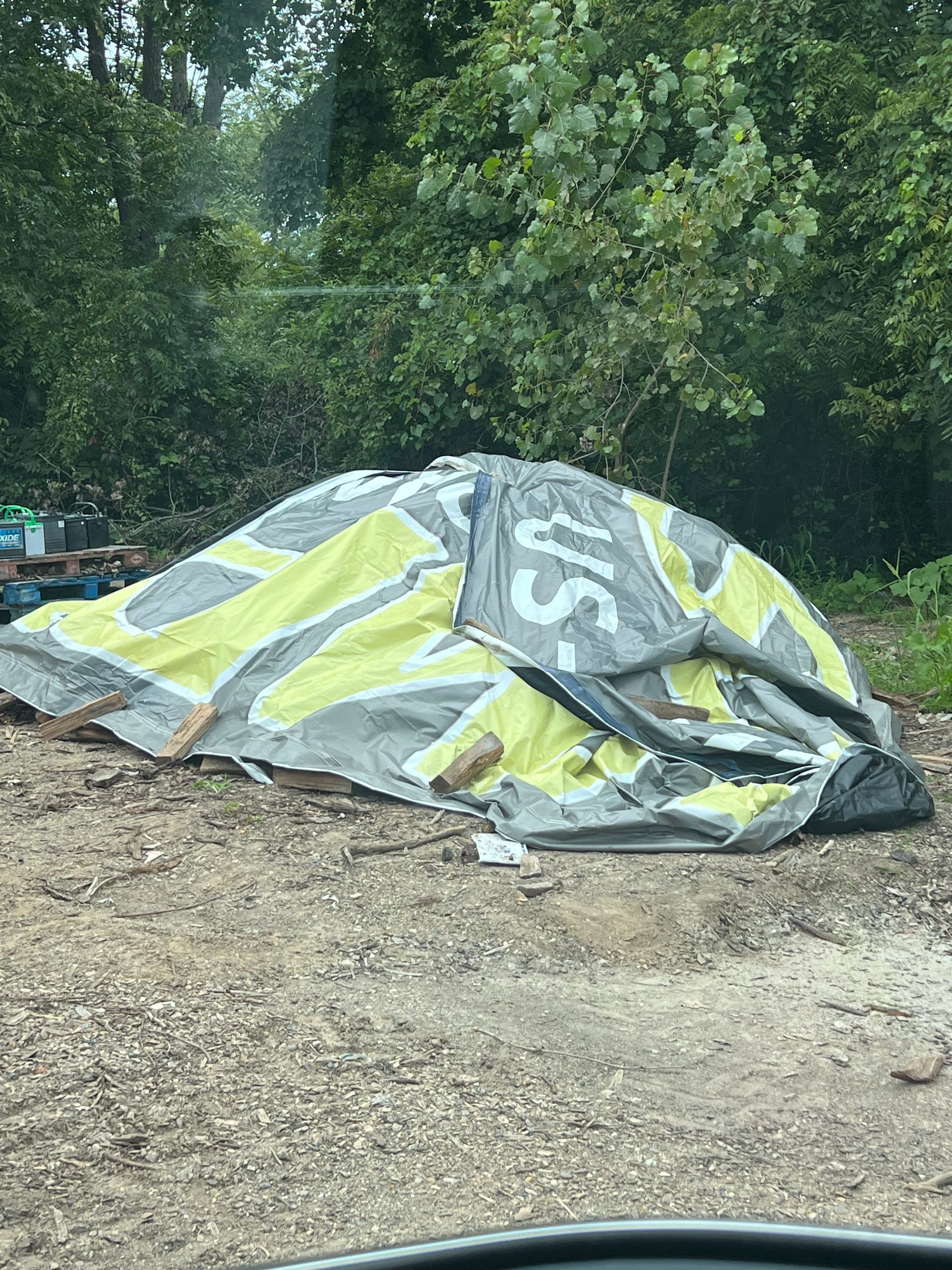 Collapsed tent with yellow and gray design on gravel path, surrounded by trees.