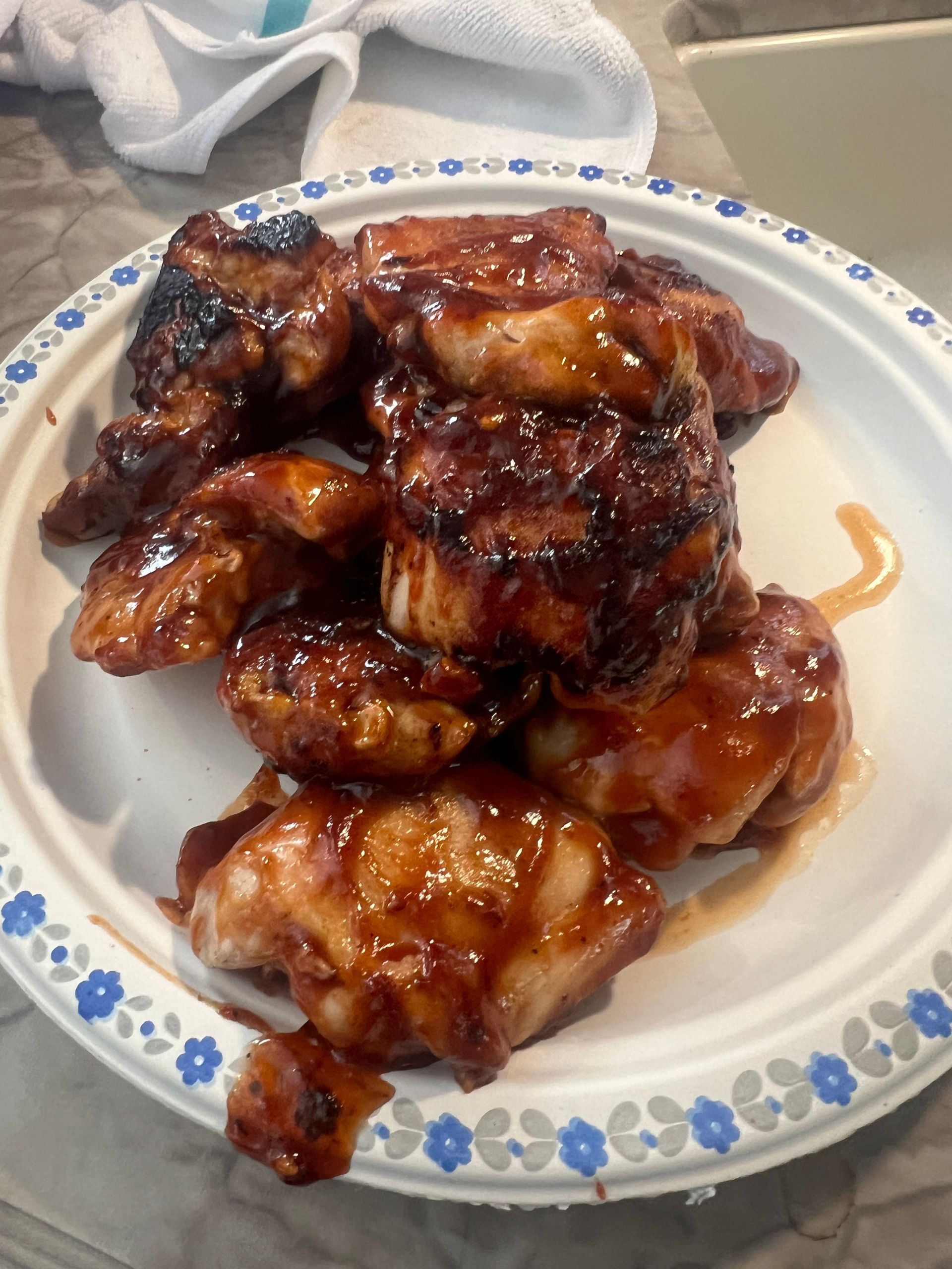 Chicken wings with dark glossy sauce on a white paper plate with blue floral trim.