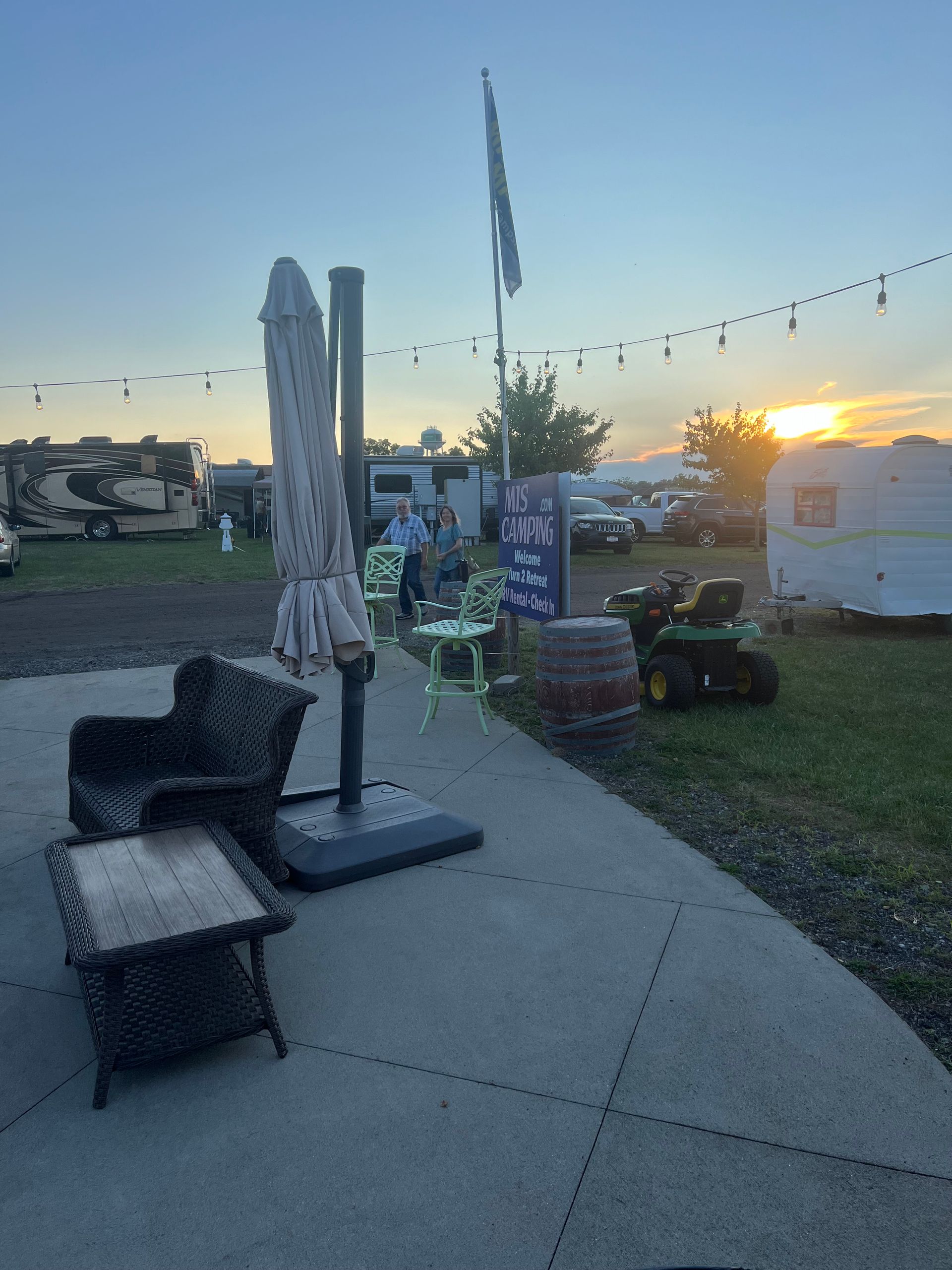 Outdoor patio with furniture, umbrella, and RVs in a campground setting at sunset.