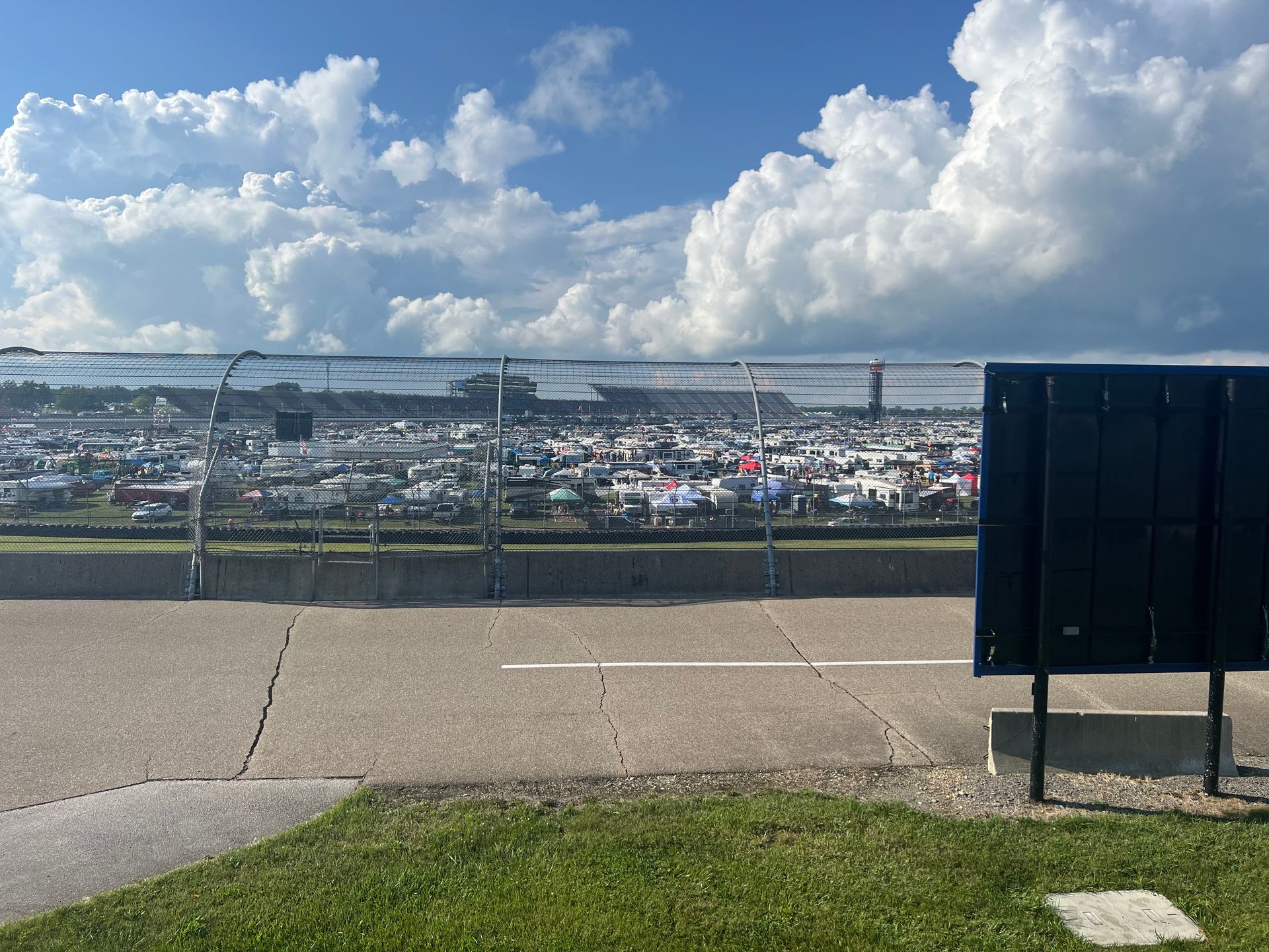 View from a paved area, overlooking a crowded racetrack under a cloudy sky.