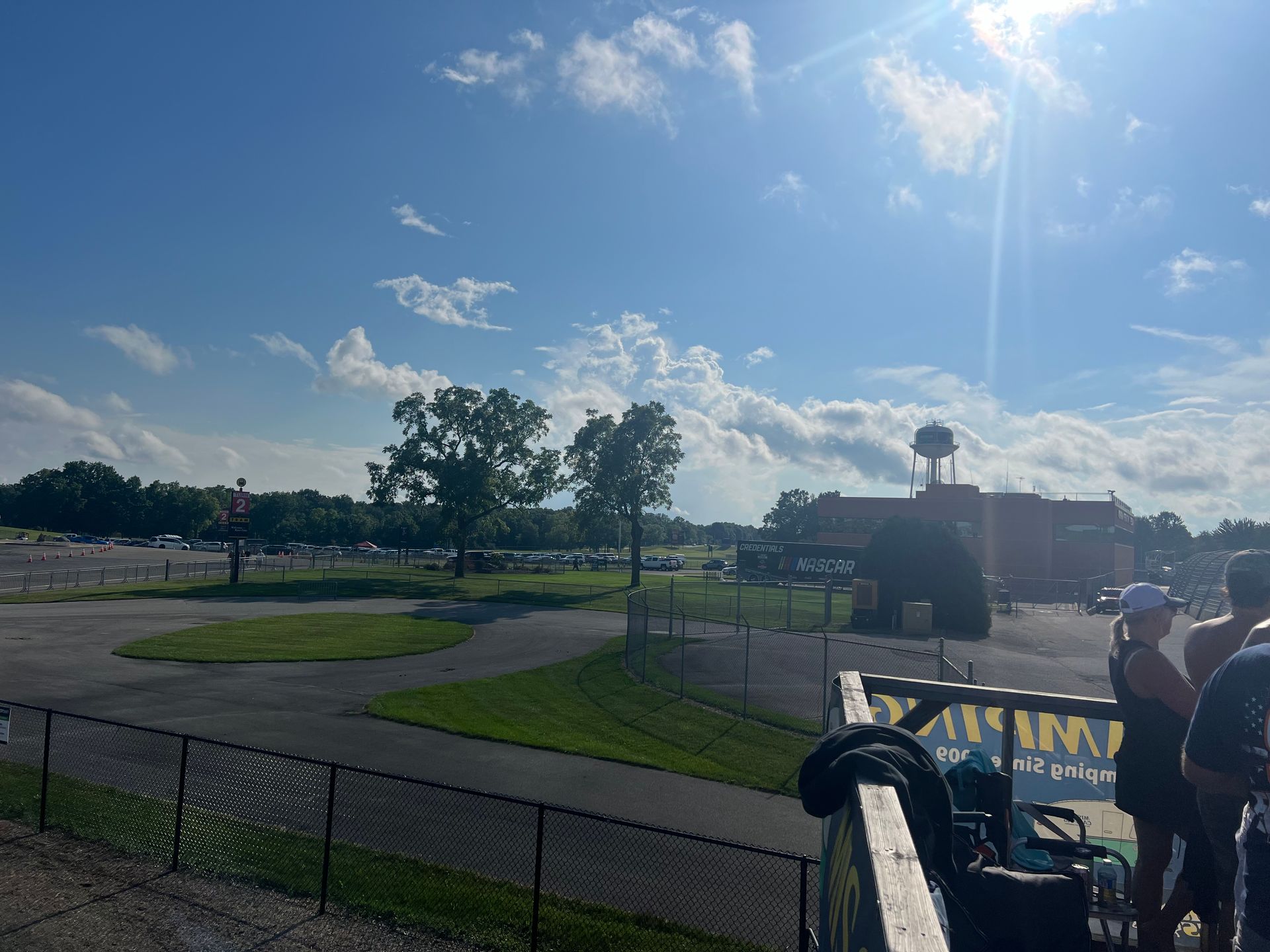 Blue sky over a park with trees, a parking lot, and people near a wooden structure.