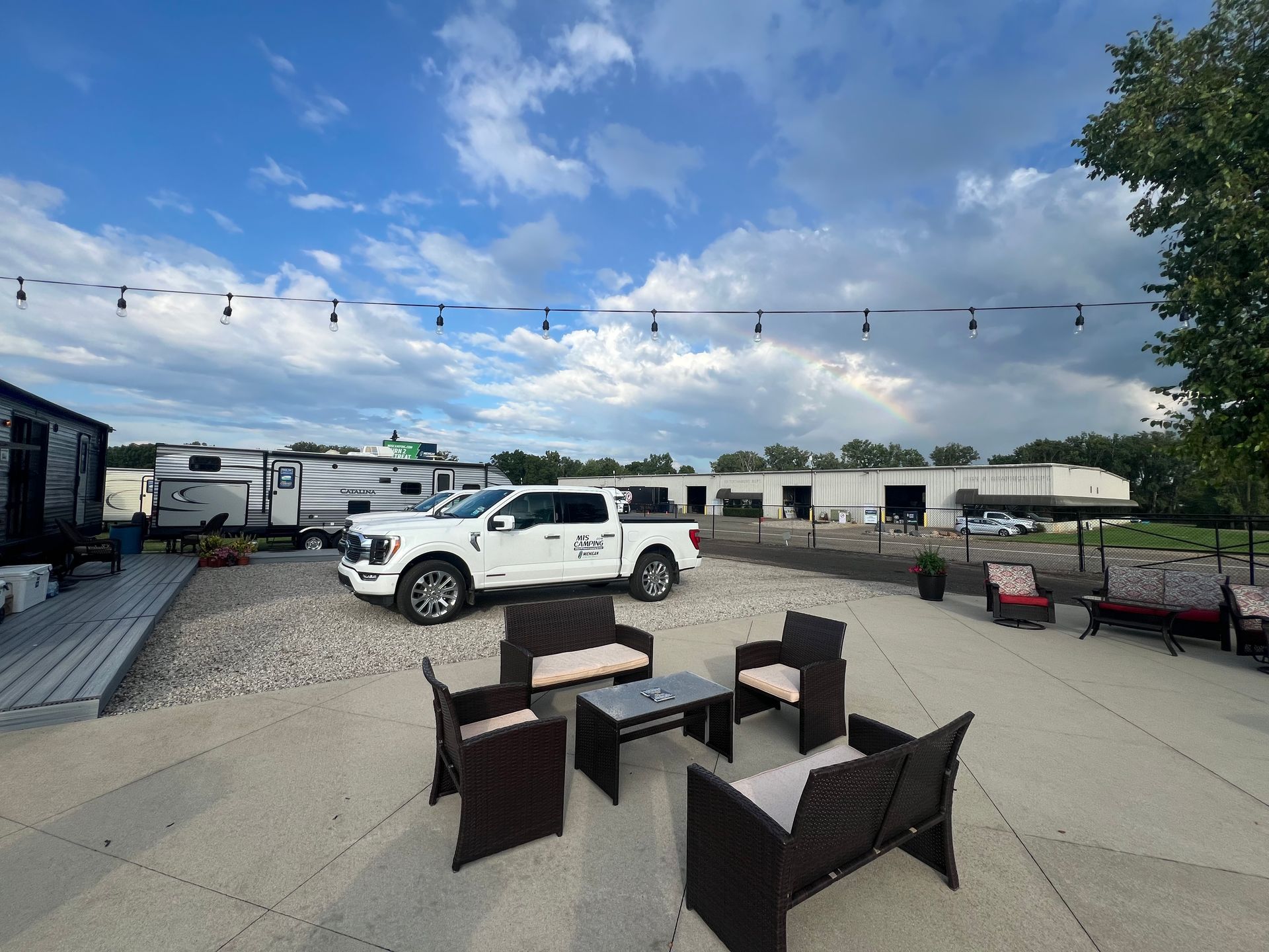 Outdoor patio with seating, truck, RVs, buildings, and a cloudy sky.