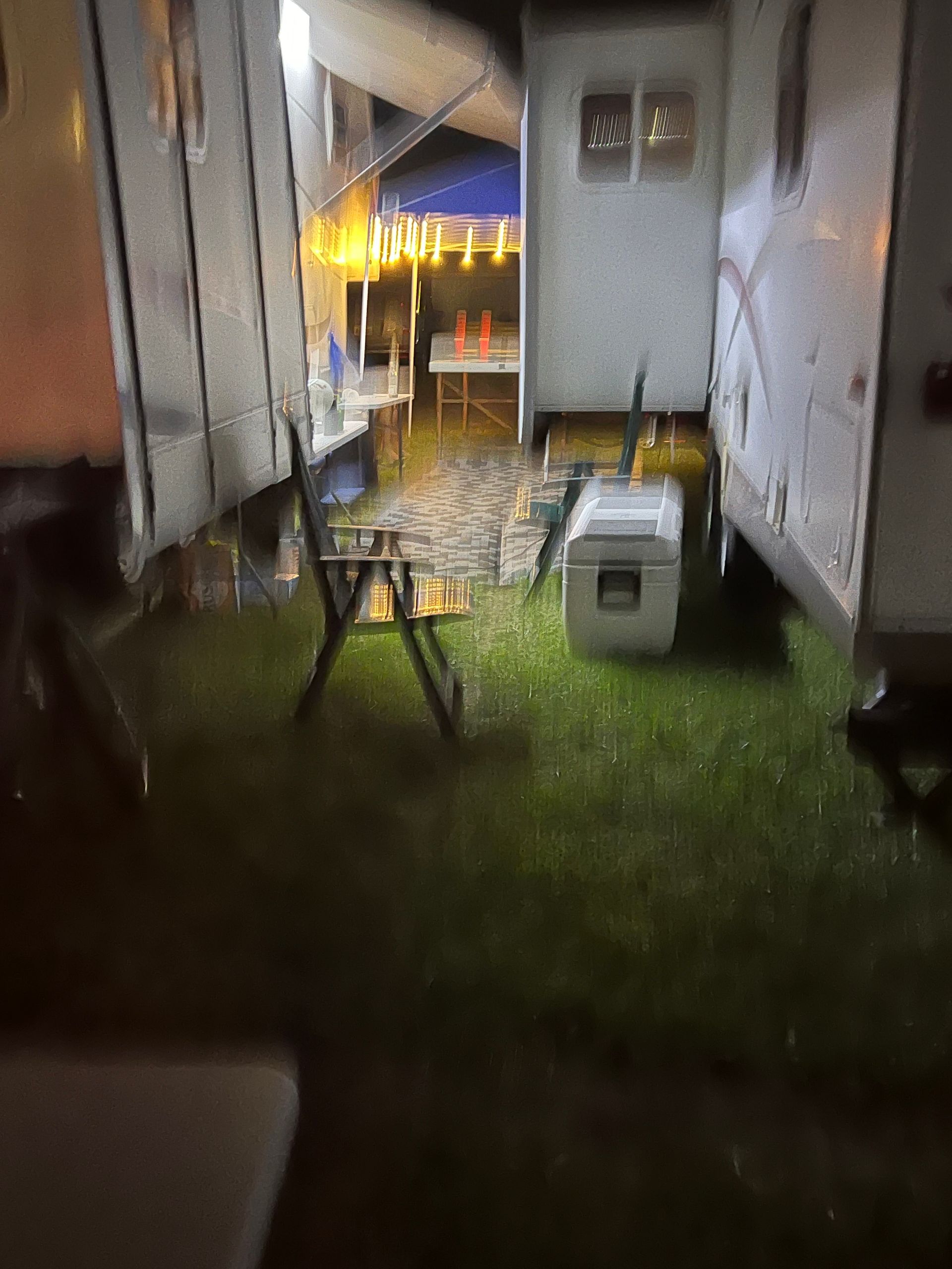 Flooded campsite between trailers, a table and chairs sit in water. Night.
