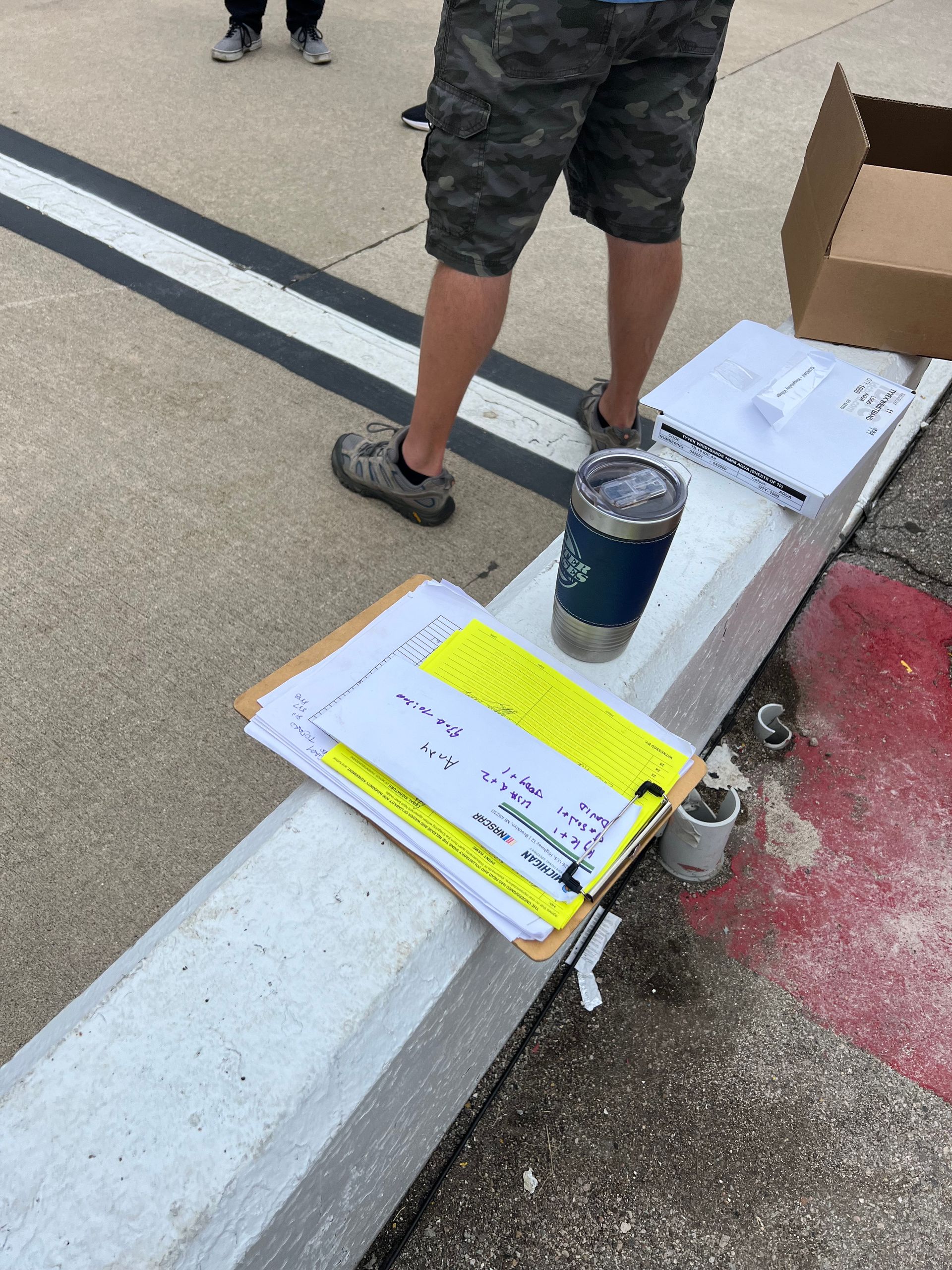 Person standing near a concrete barrier holding paperwork, a tumbler, and spray paint.