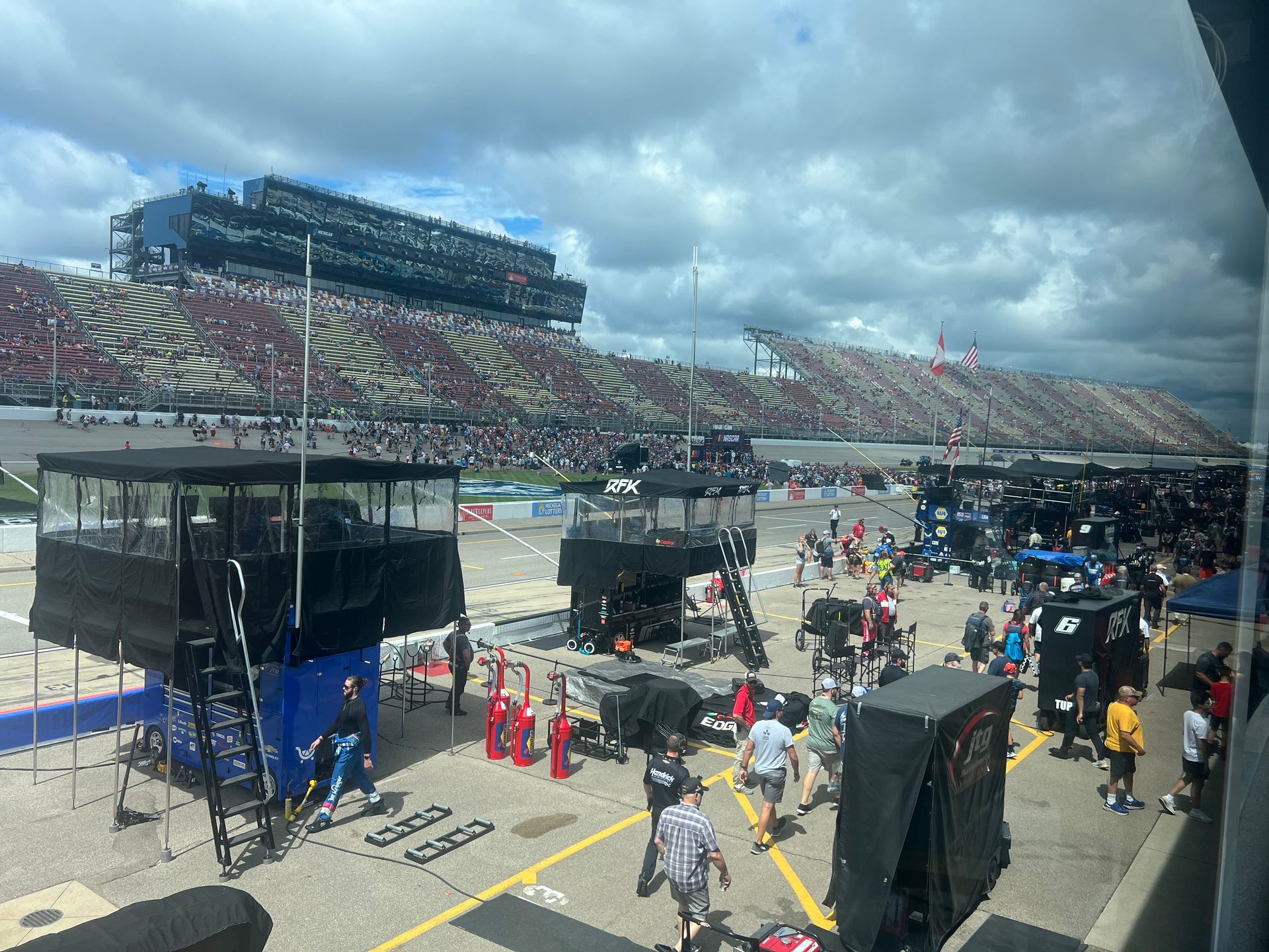 Race track scene with crowd in stands, pit crew working, and black structures.