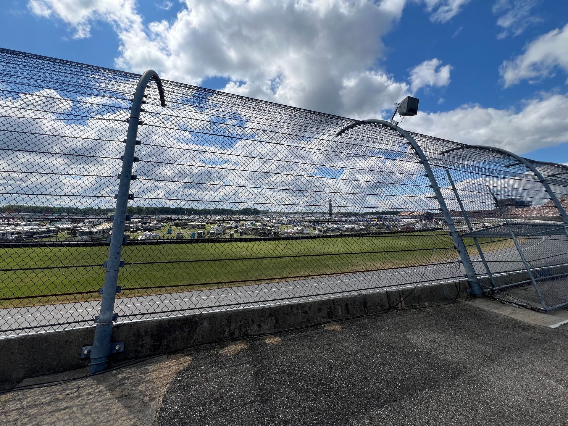Metal fence with an arched top, against a green field and a blue sky with clouds.