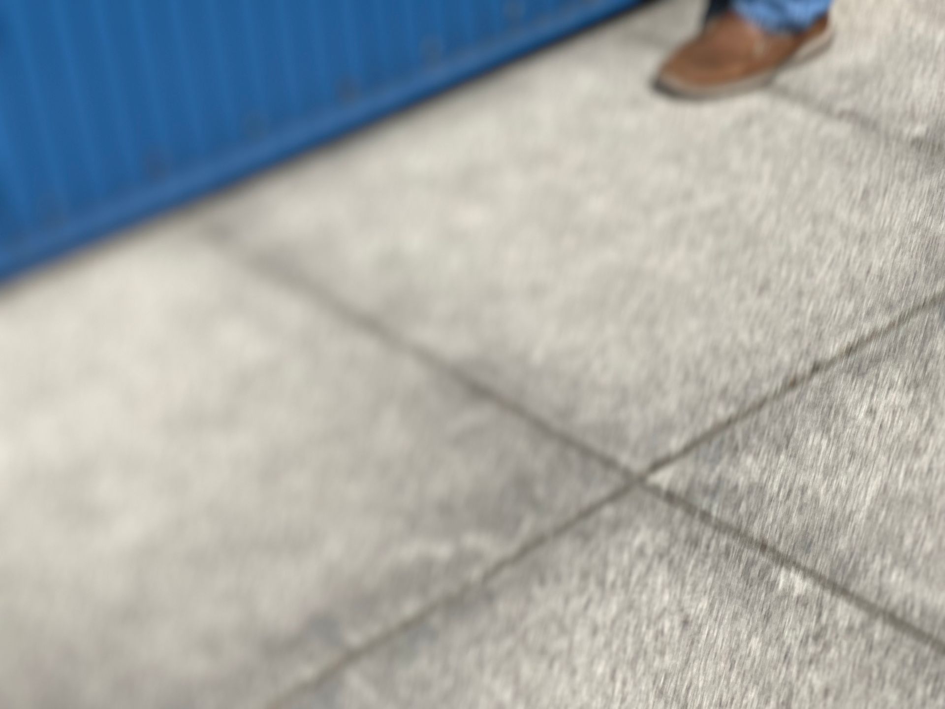 Person in jeans and brown shoe standing by a blue barrier, concrete ground.