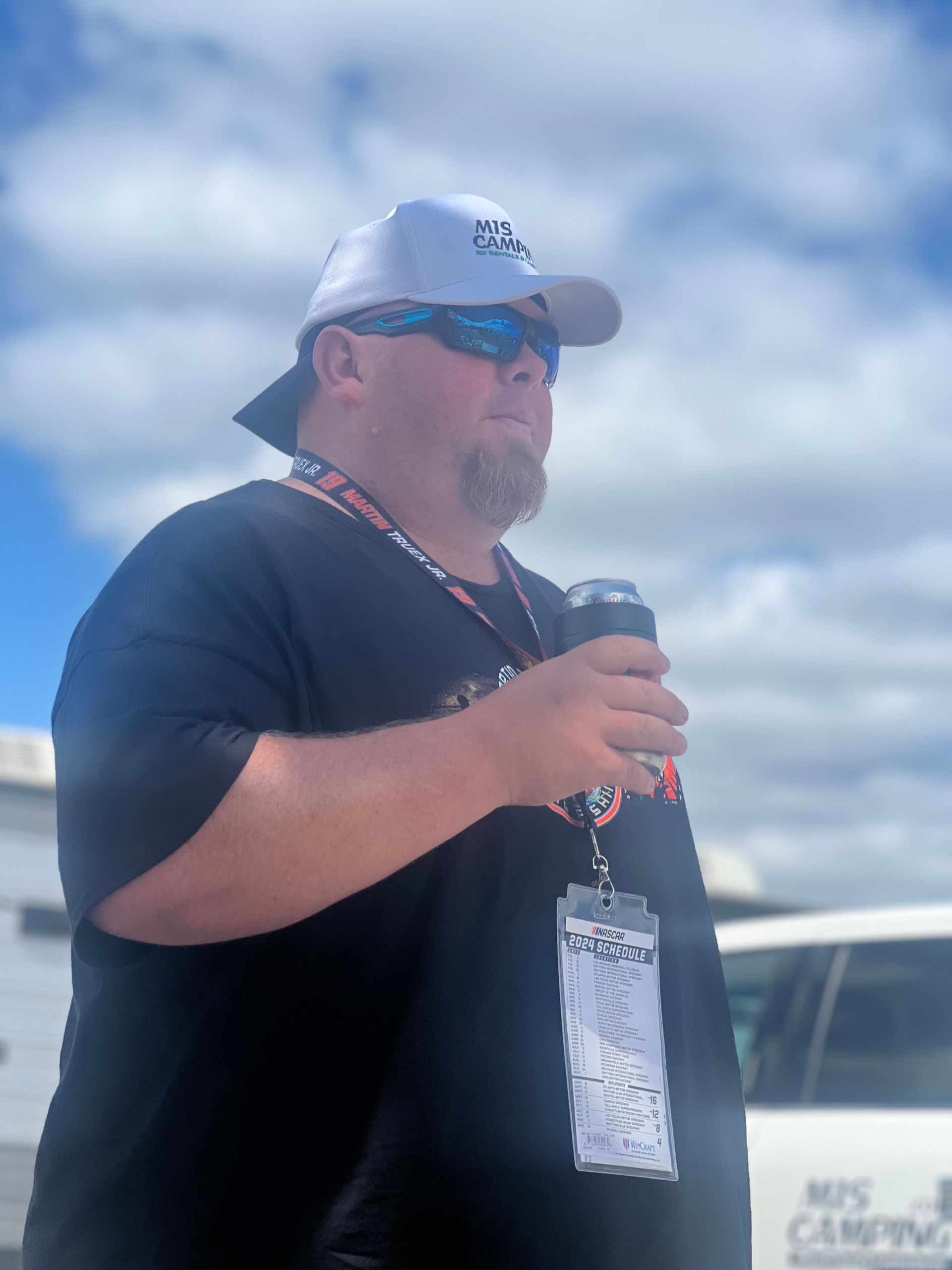 Man in black shirt and hat, holding a can, looking to the side under a blue sky.