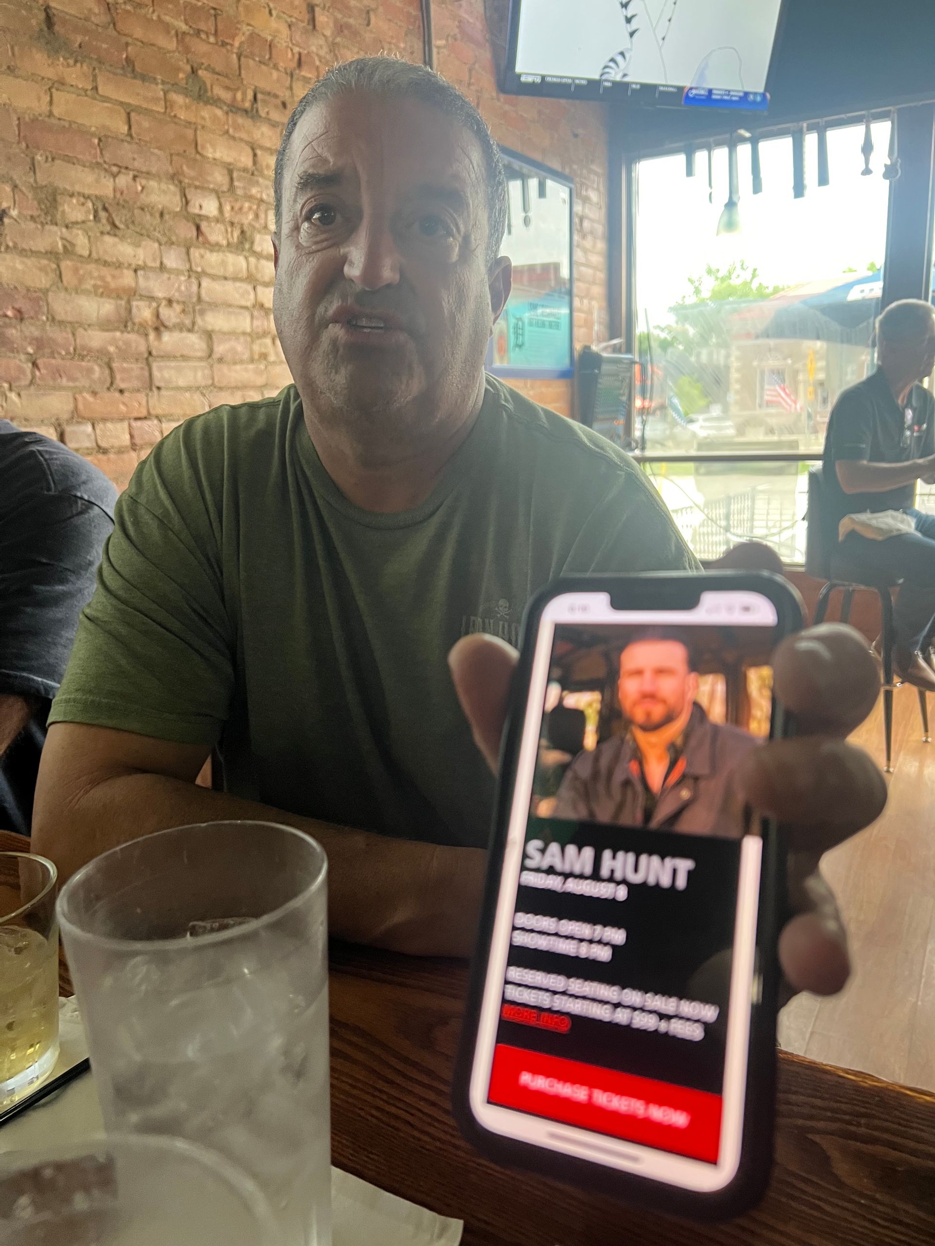 Man holding phone with Sam Hunt's photo and information at a bar.