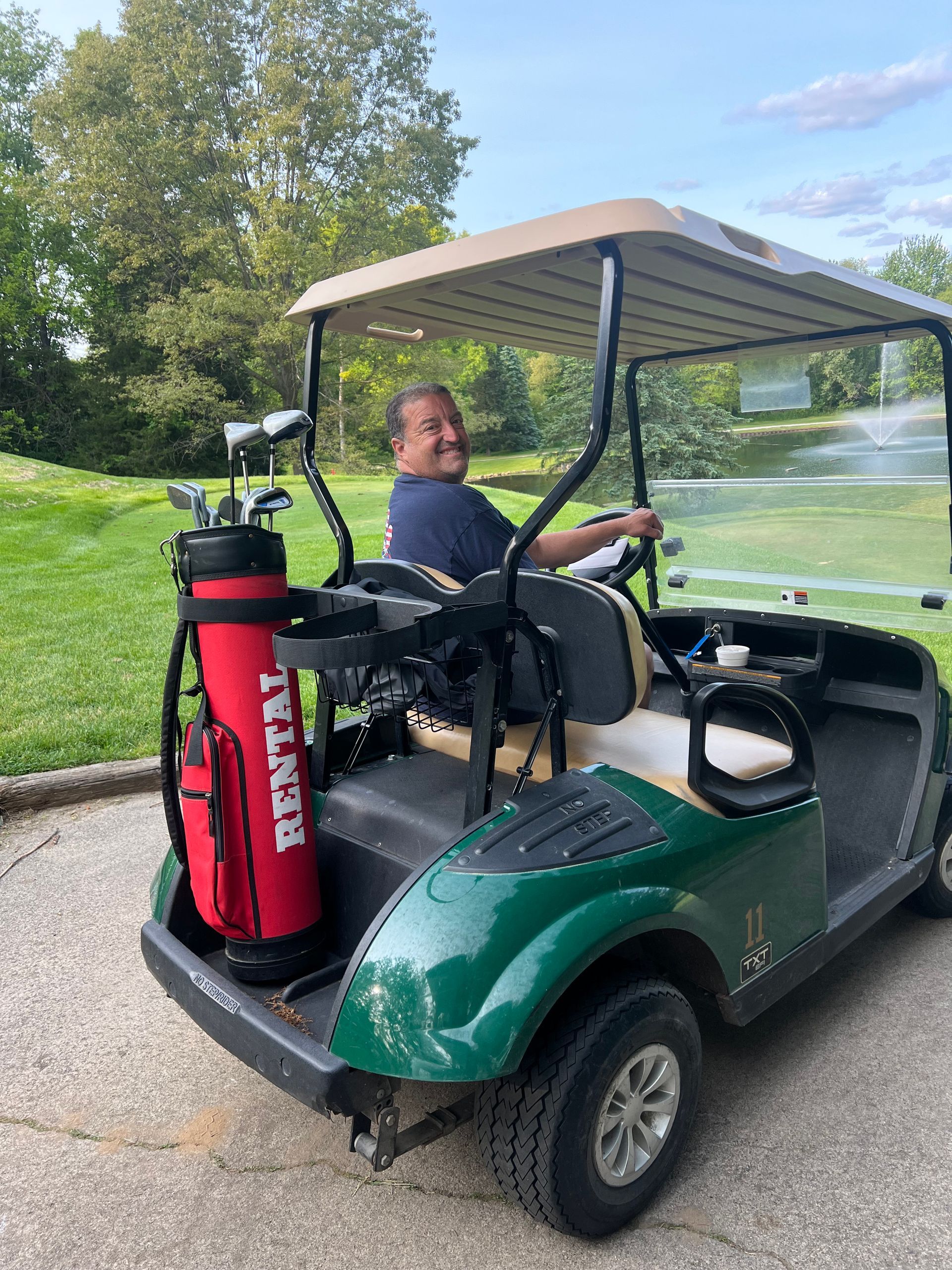 Man driving a green golf cart with a red 