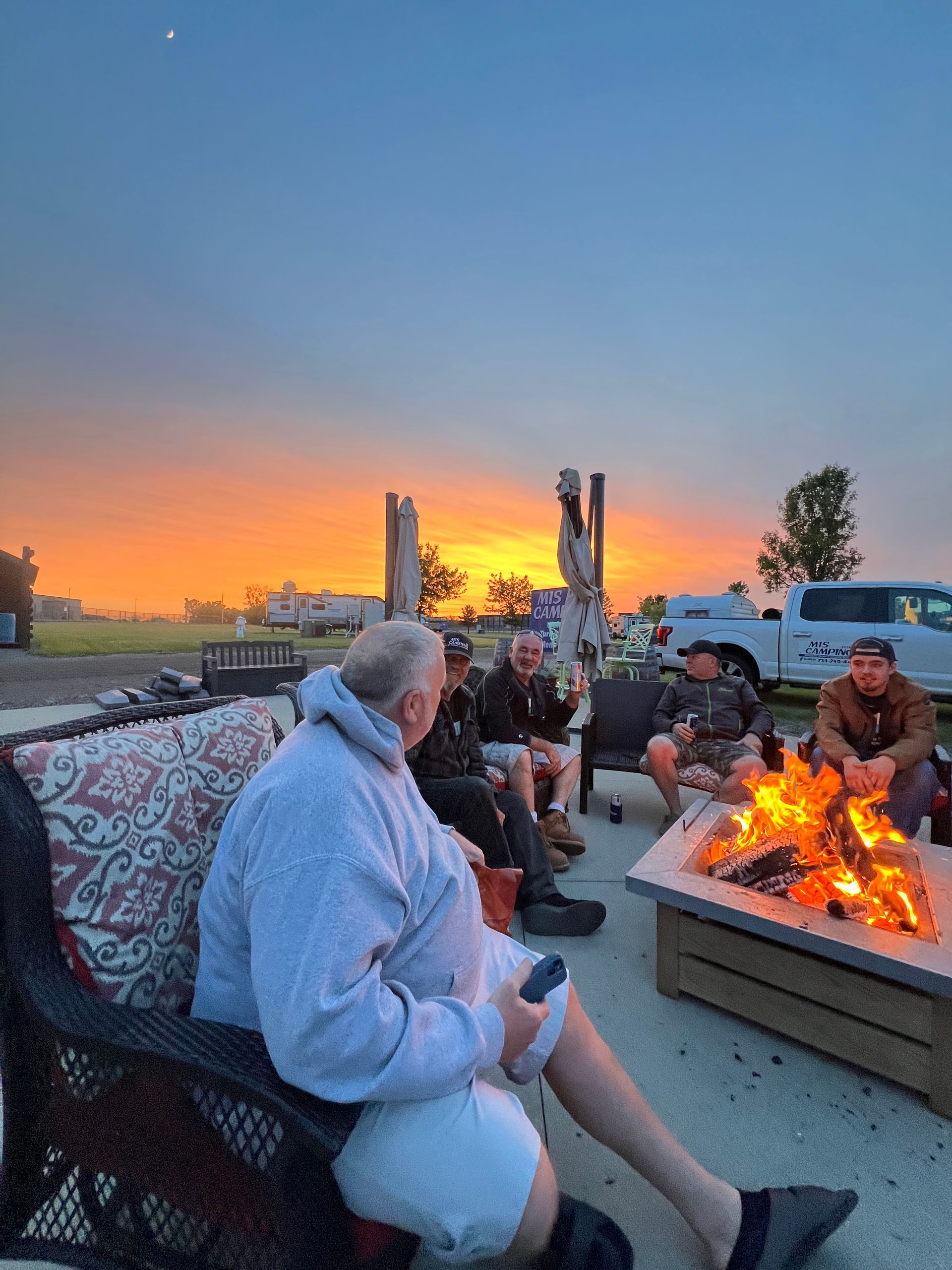 People around a fire pit at sunset, enjoying drinks and conversation.