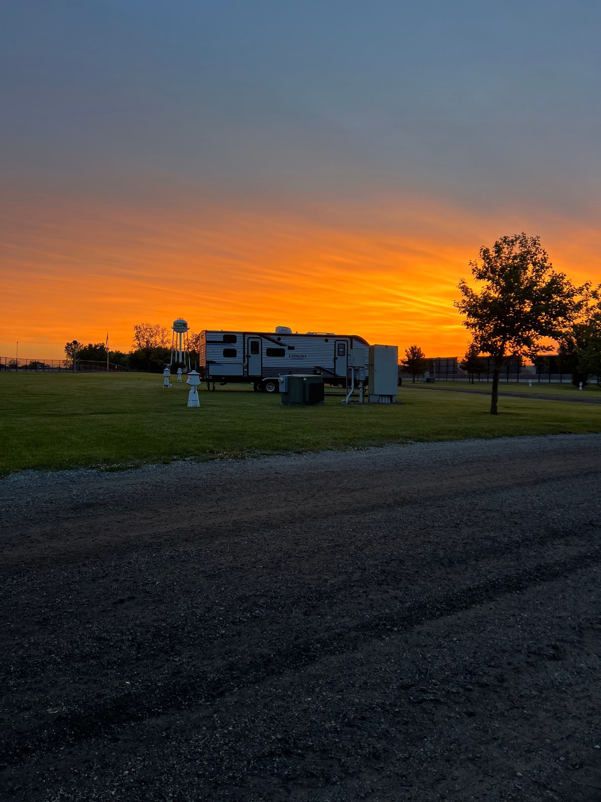 RV parked in grassy campsite at sunset, with an orange and yellow sky above.