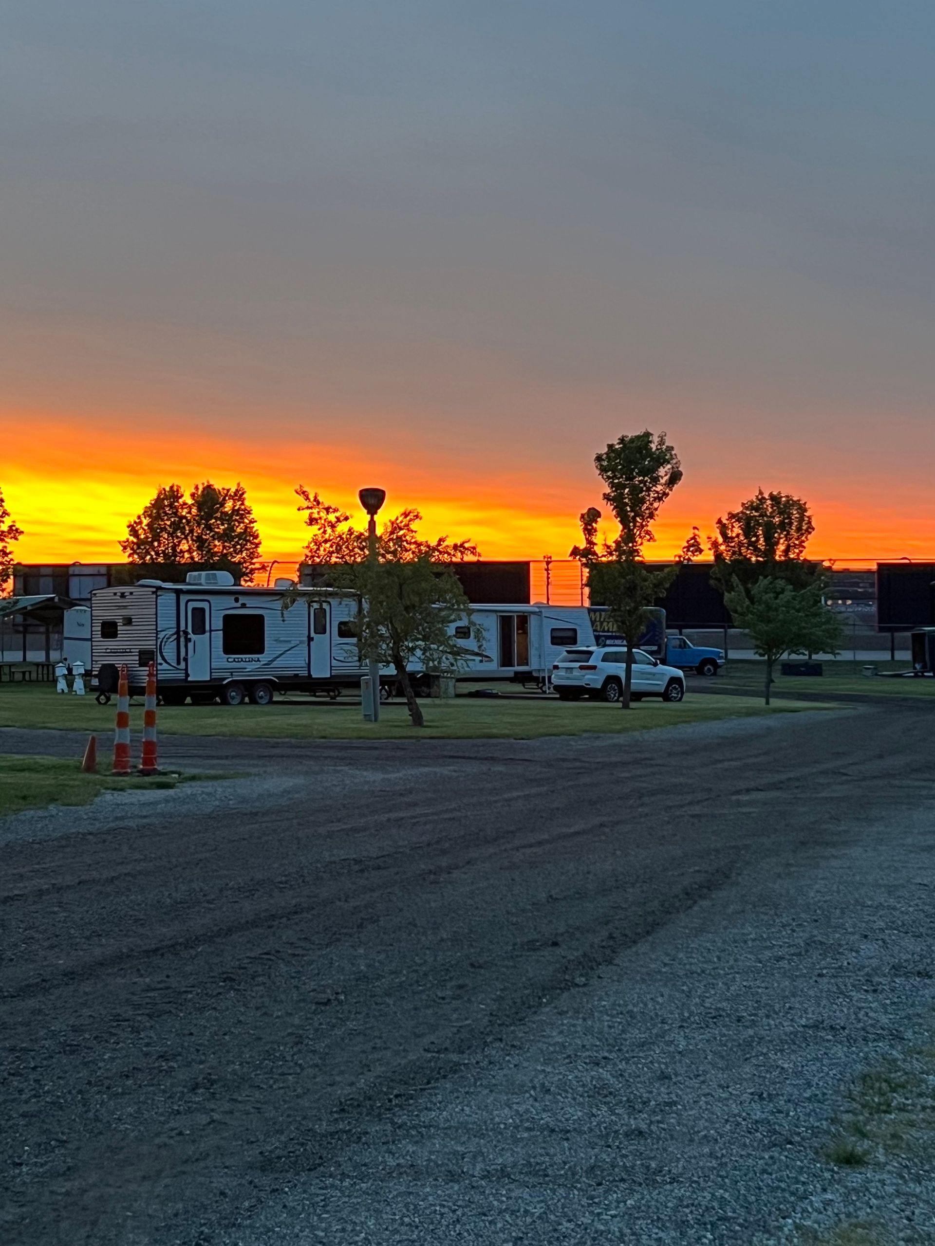 Campground at sunset, trailers parked on gravel, orange and yellow sky.