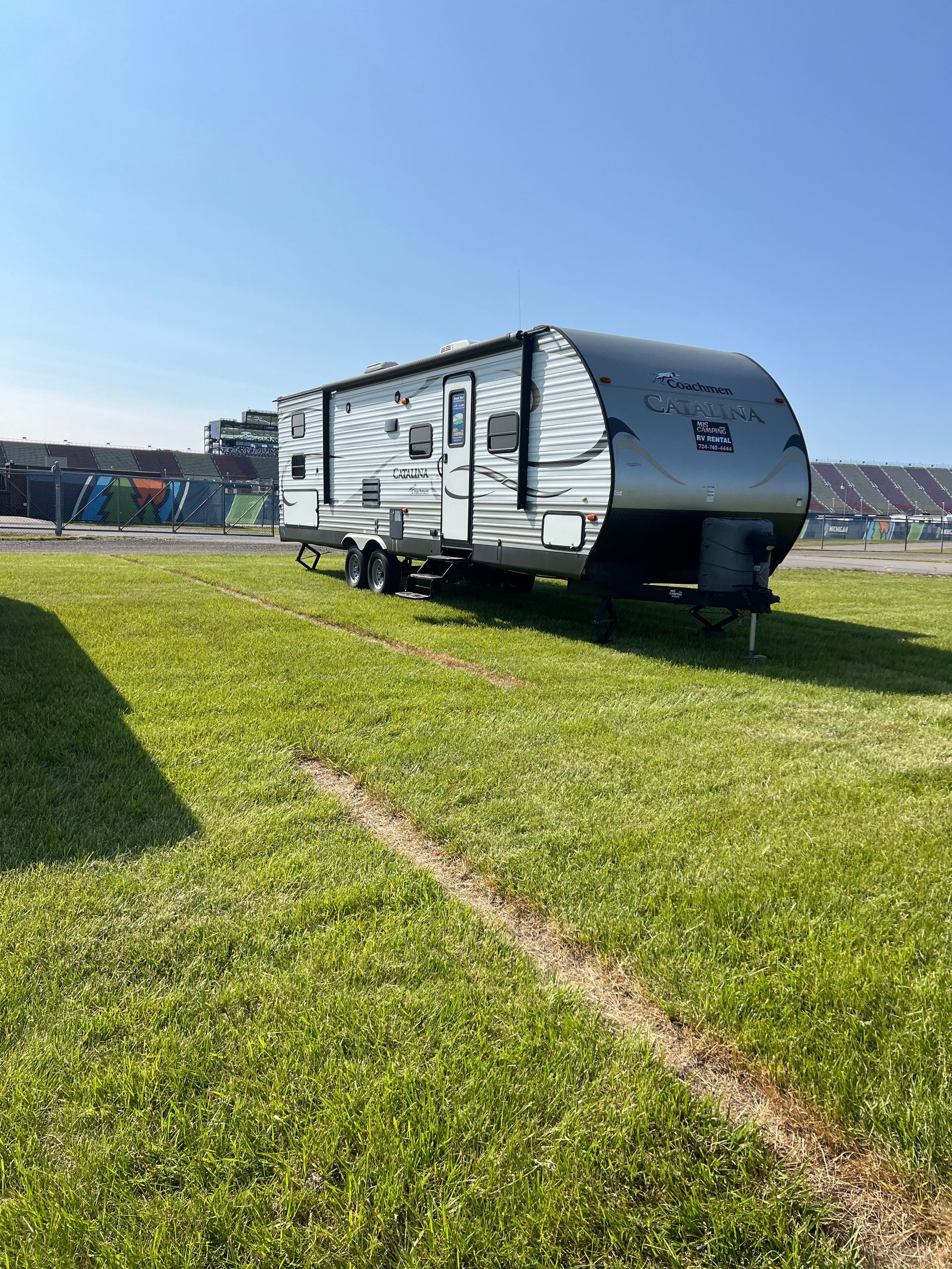 RV trailer parked on infield under a clear, blue sky.