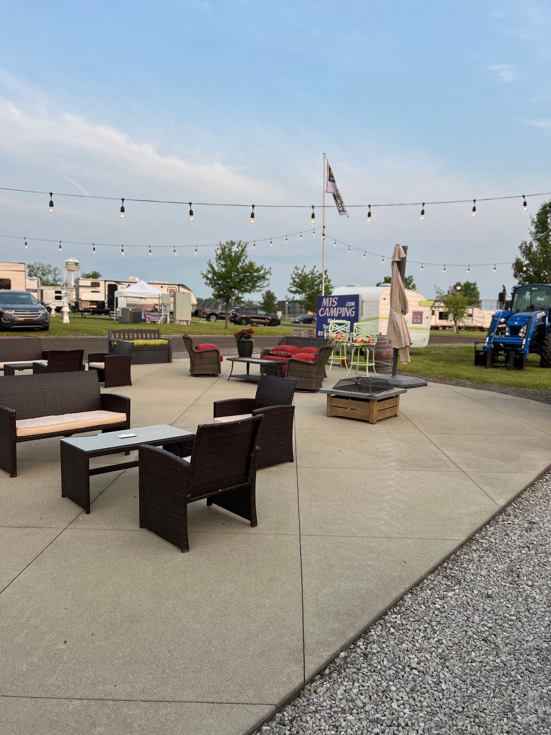 Outdoor patio seating area with string lights, gravel border, and RVs in the background.