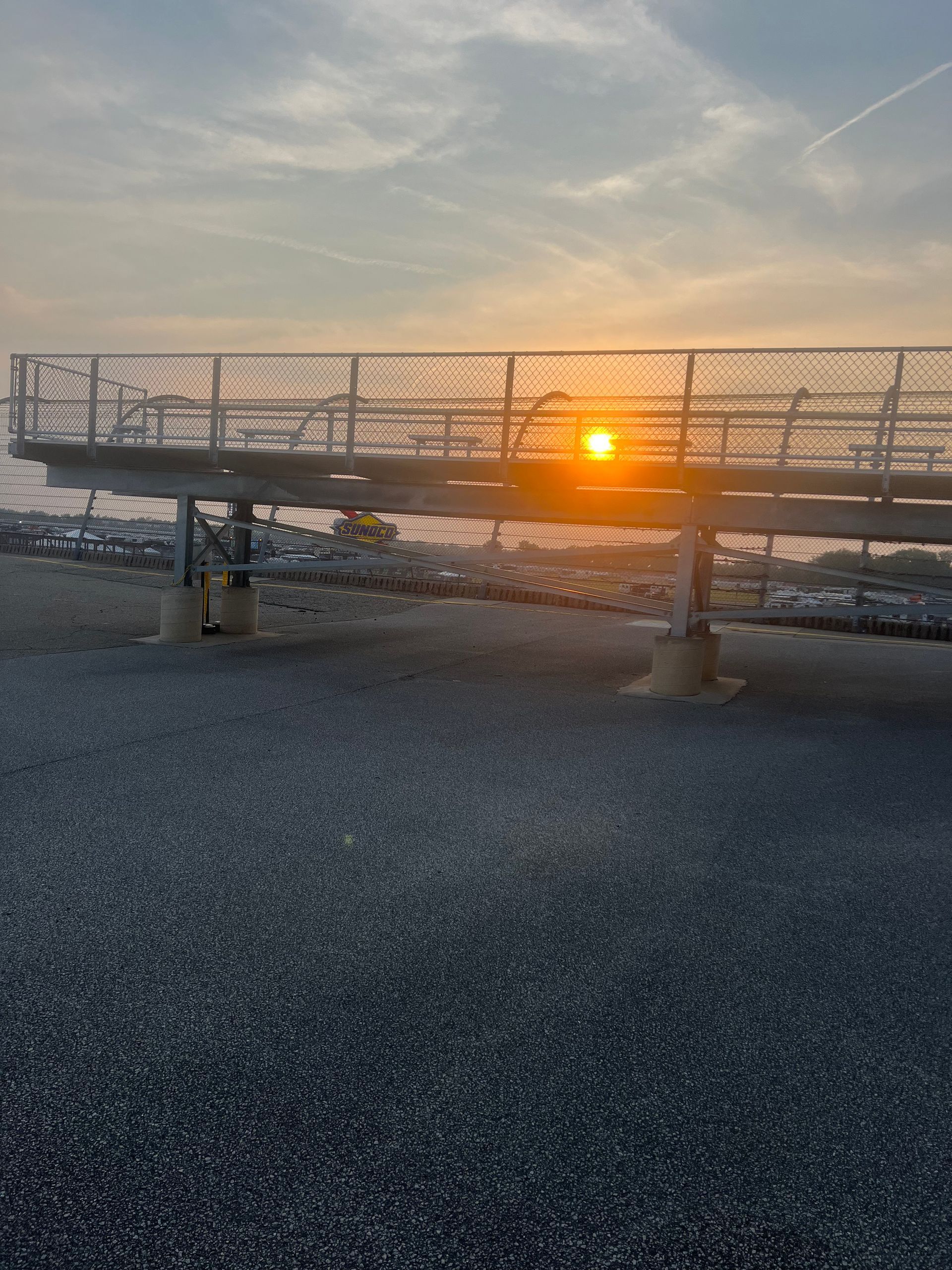 Sunset through a metal structure on a pebble surface, with contrails in the sky.