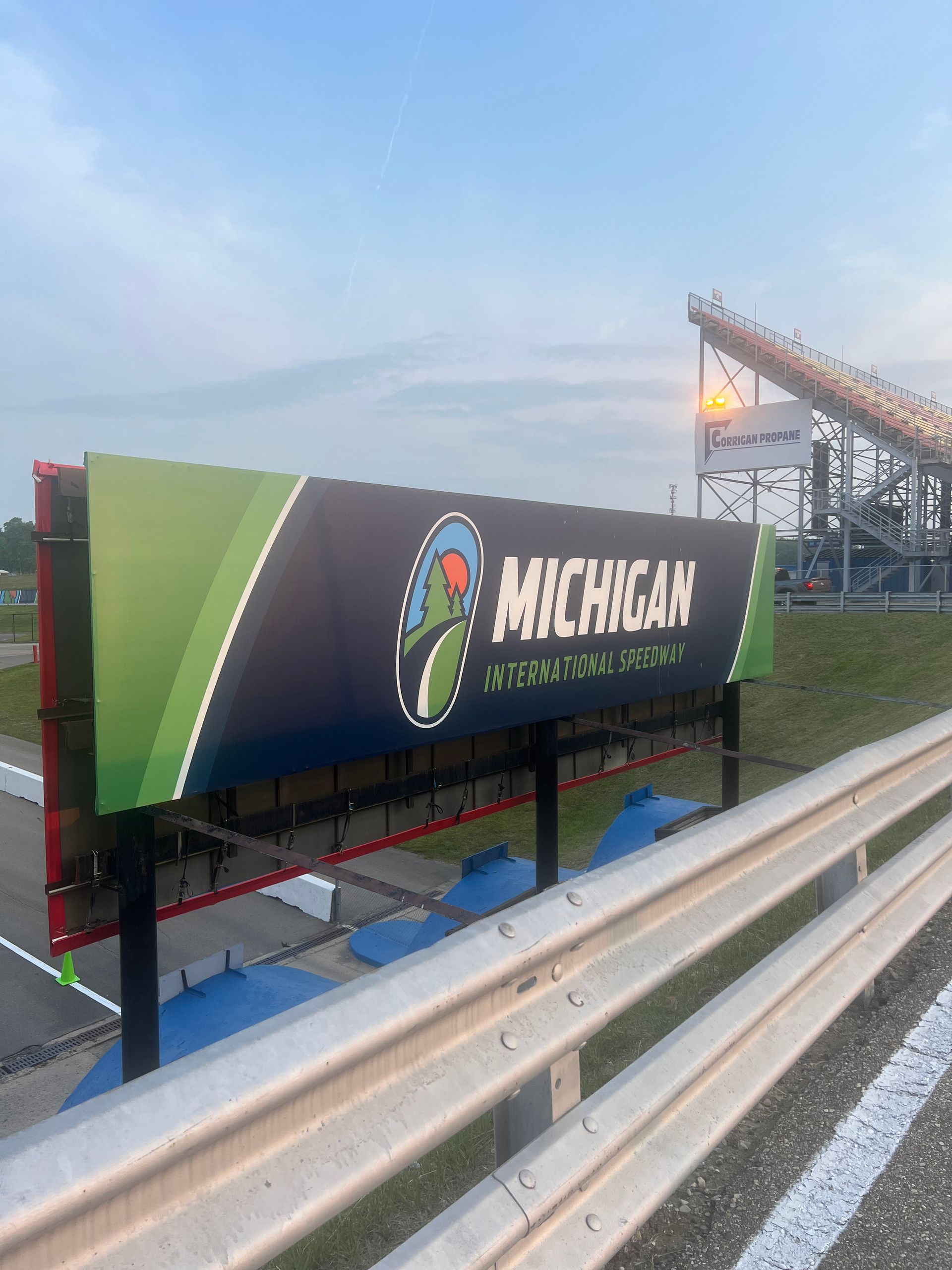 Sign at Michigan International Speedway with the track and a grandstand visible.