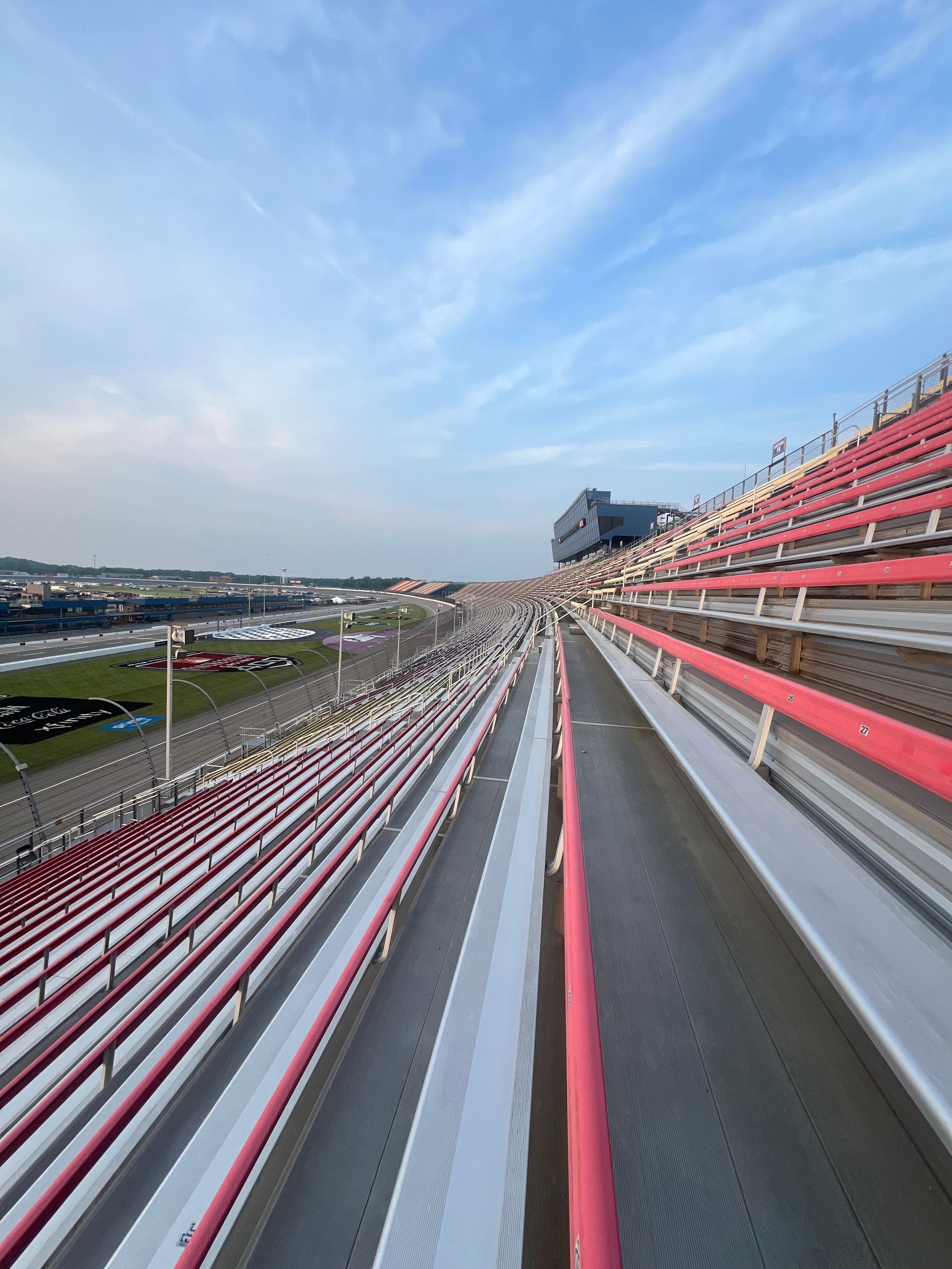 Empty race track grandstands with red and white seats, and track below under a cloudy sky.
