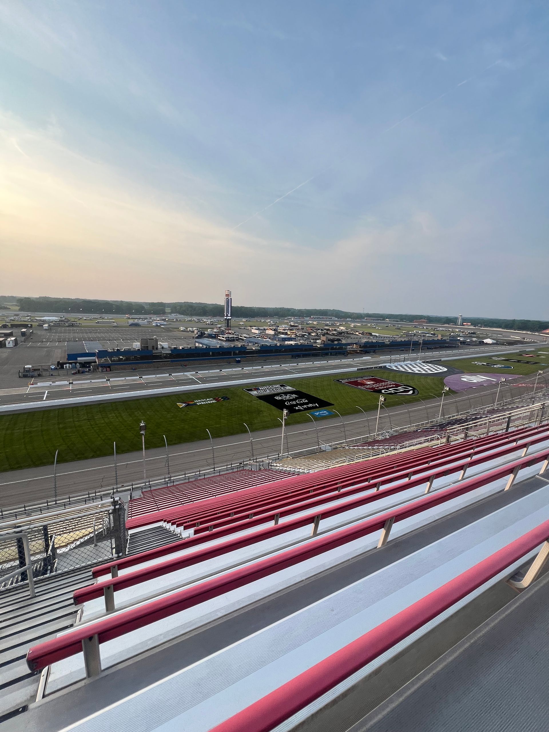 Race track grandstand with red seats, overlooking the track and facilities under a blue sky.