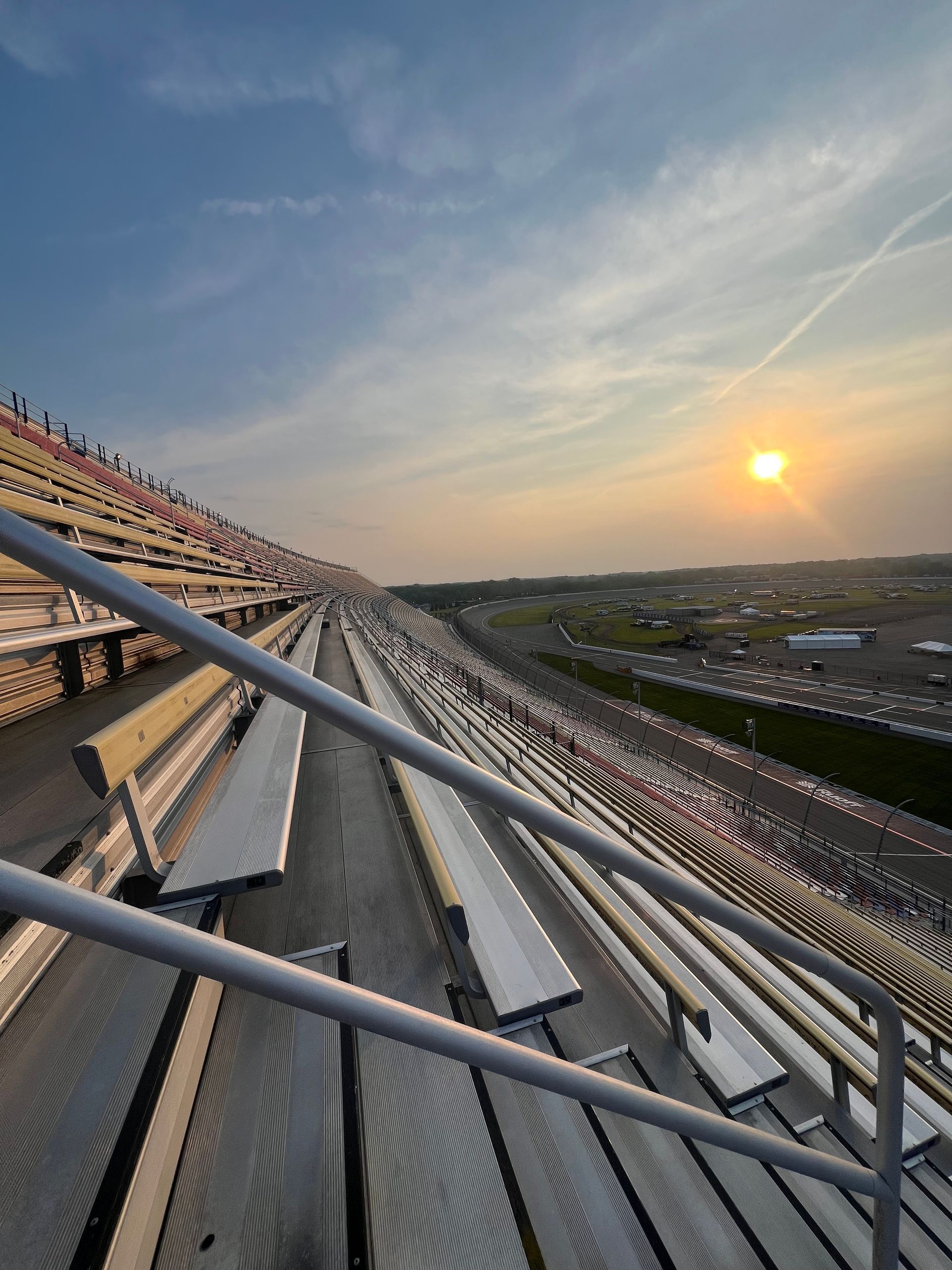 Empty stadium seats at sunset; view of the racetrack and parking area in the distance.
