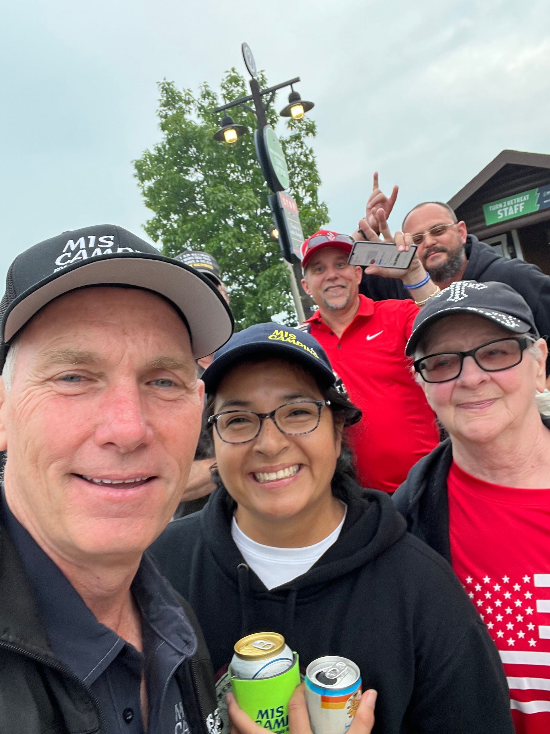Group of people smiling, posing for a selfie outside a restaurant, holding drinks.
