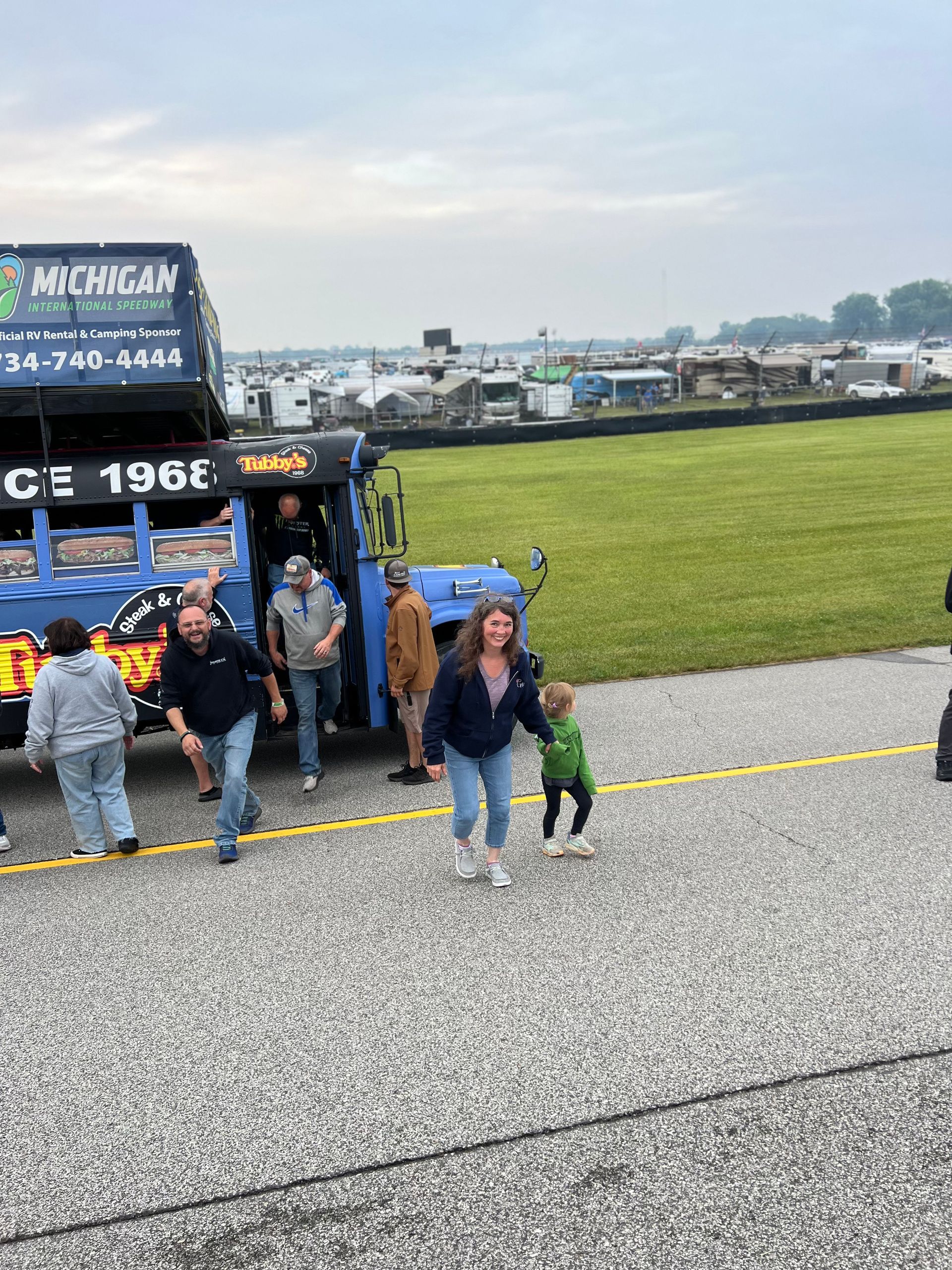 People exiting a blue tow truck on a paved surface near a grassy field and buildings.