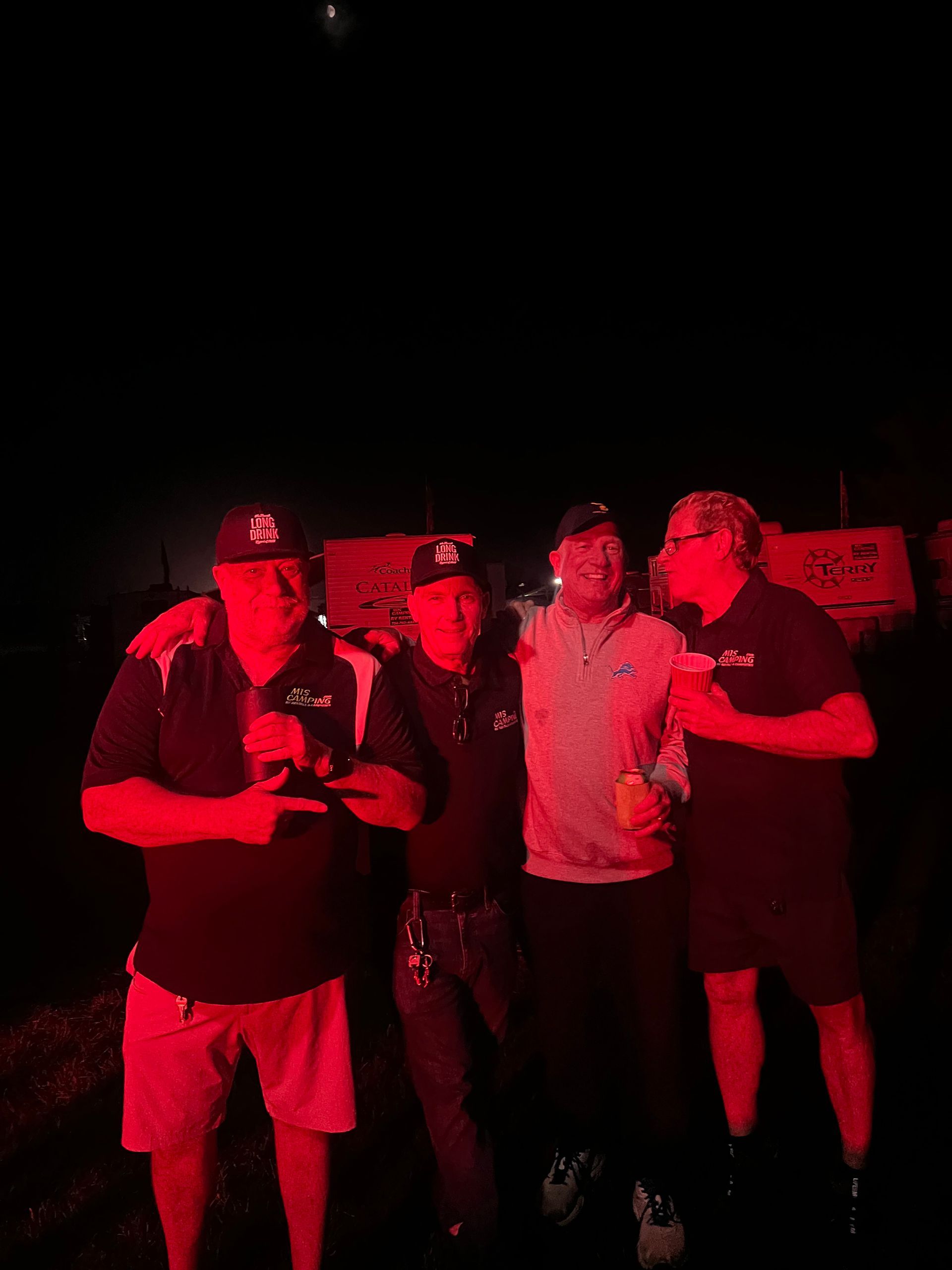 Four people in hats and dark clothing illuminated by red light at night.