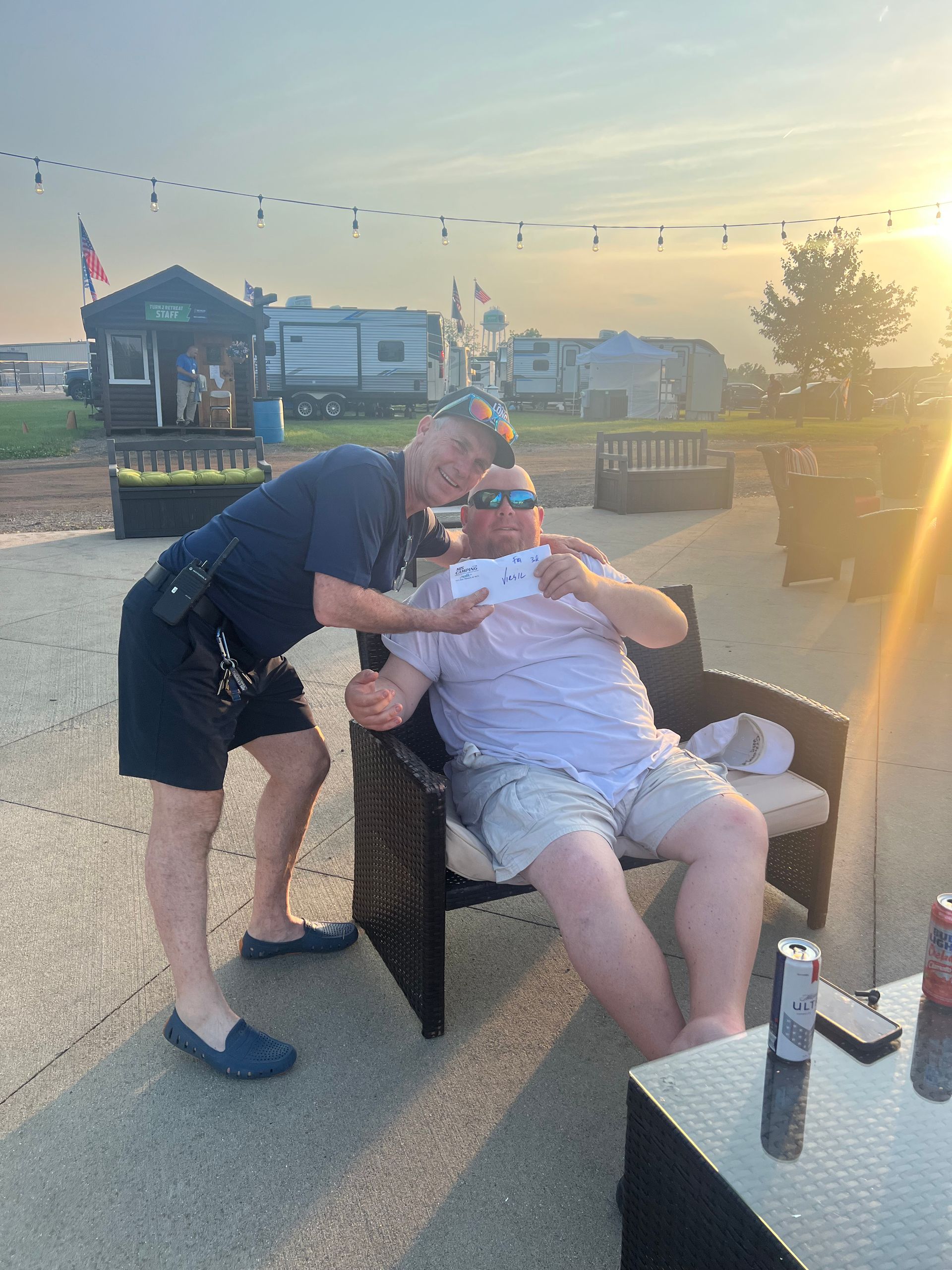 A uniformed person kissing a person on the cheek while they hold a paper outdoors near RVs.