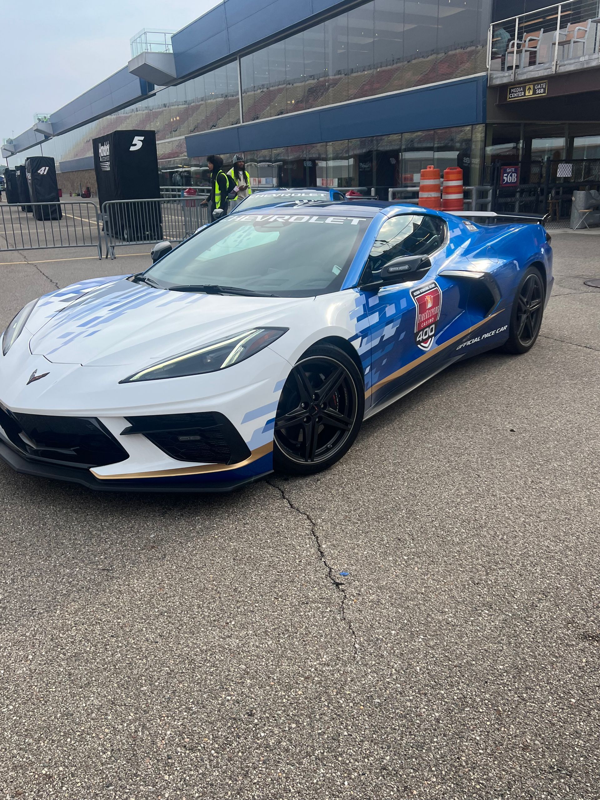 White and blue police-themed Corvette on a race track, with a grandstand in the background.